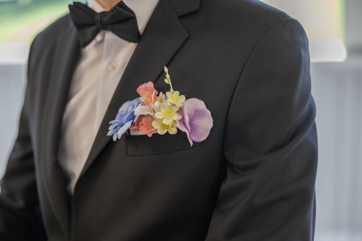 Close-up of a groom in a black tuxedo with a colorful floral boutonniere in his breast pocket.