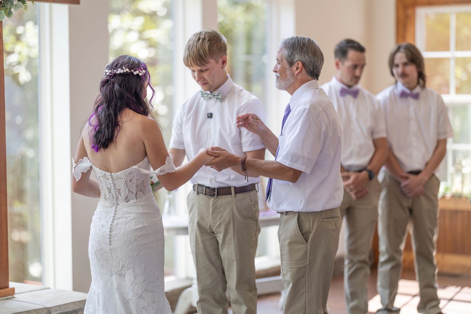 Bride and groom exchanging vows at indoor wedding ceremony with groomsmen standing in background.