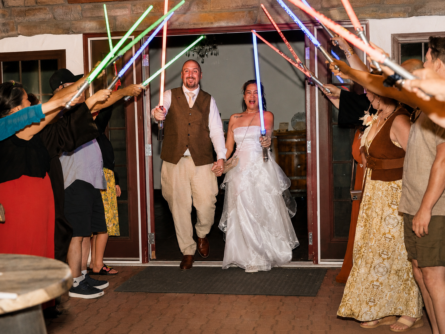 Bride and groom exit wedding reception through lightsaber arch held by guests in Star Wars themed celebration.