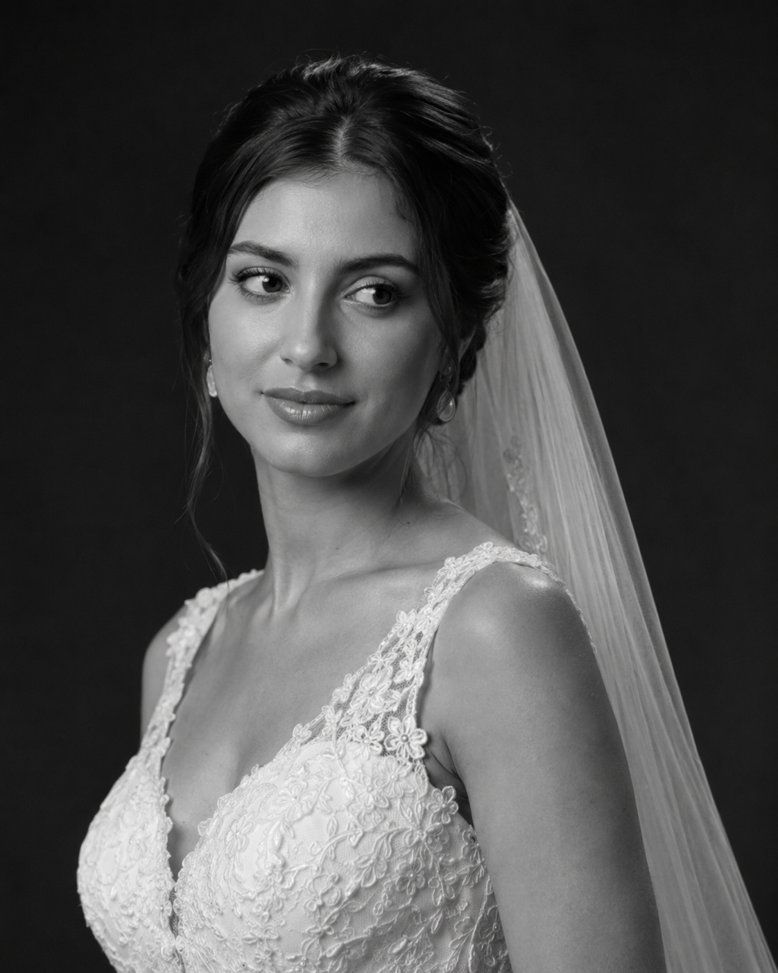 Black and white bridal portrait of a woman in a lace wedding dress and veil, elegant updo hairstyle.