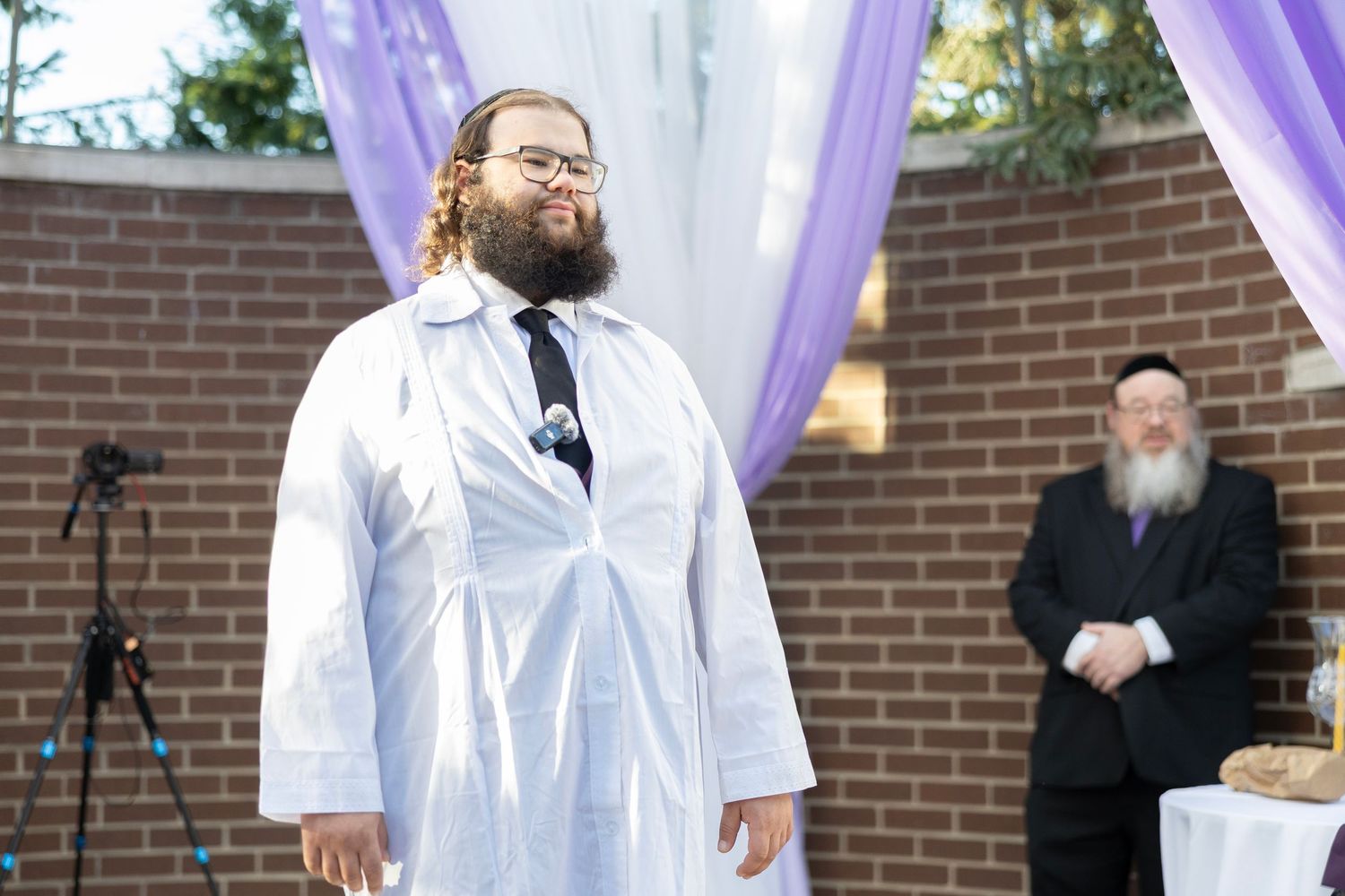 Wedding ceremony with purple drapes and decorations in front of a brick wall.