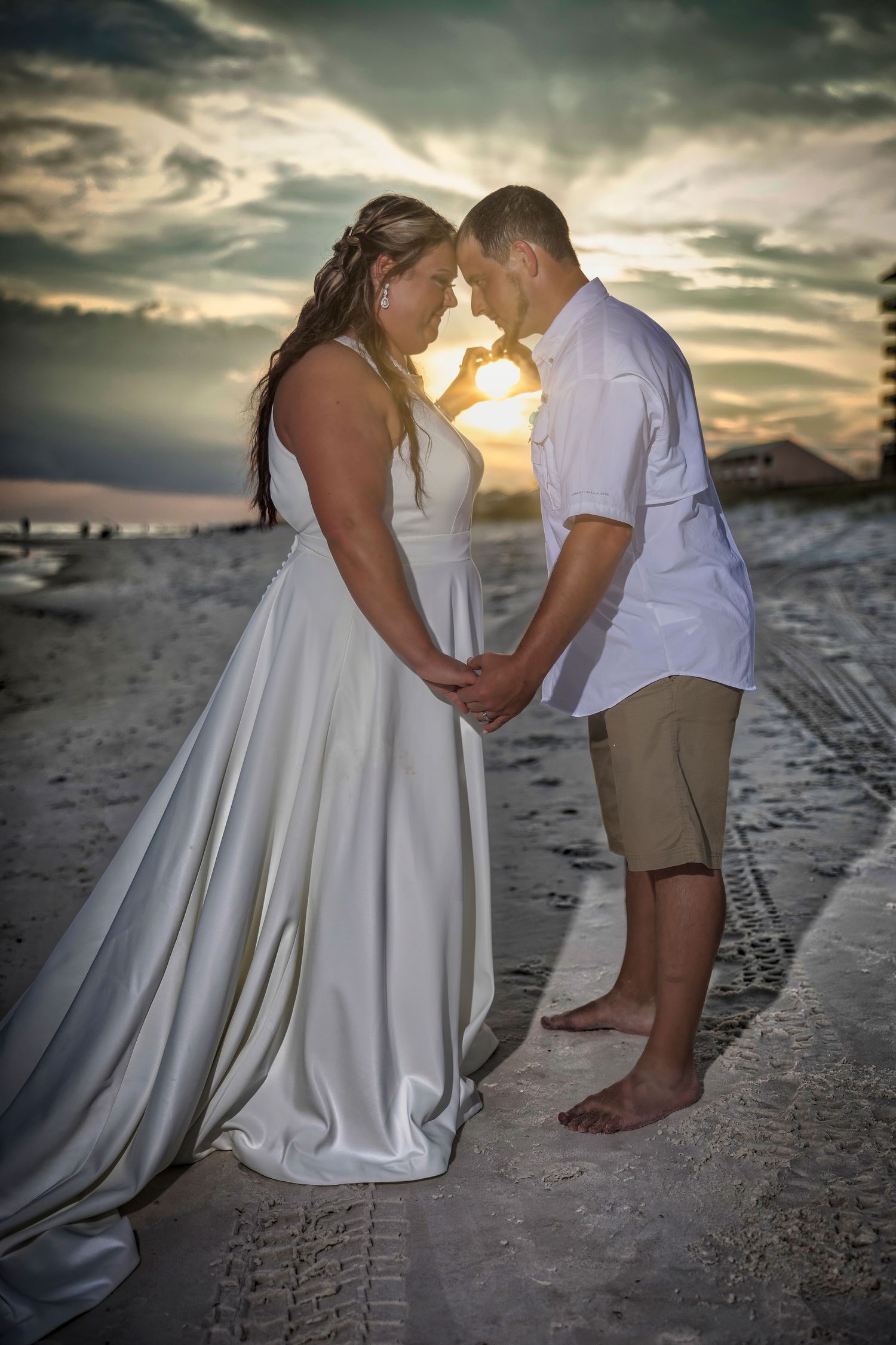 A romantic beach wedding photoshoot at sunset with a couple posing together in white attire on sandy shores.