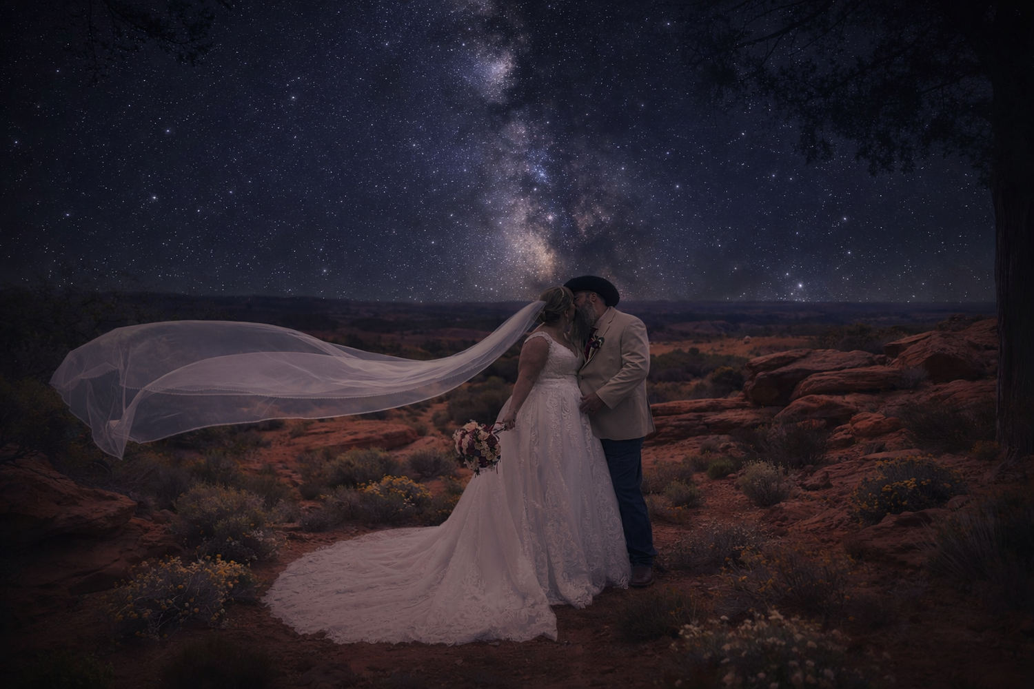 Bride and groom kiss under the Milky Way in a desert landscape, with veil flowing in the wind at night.