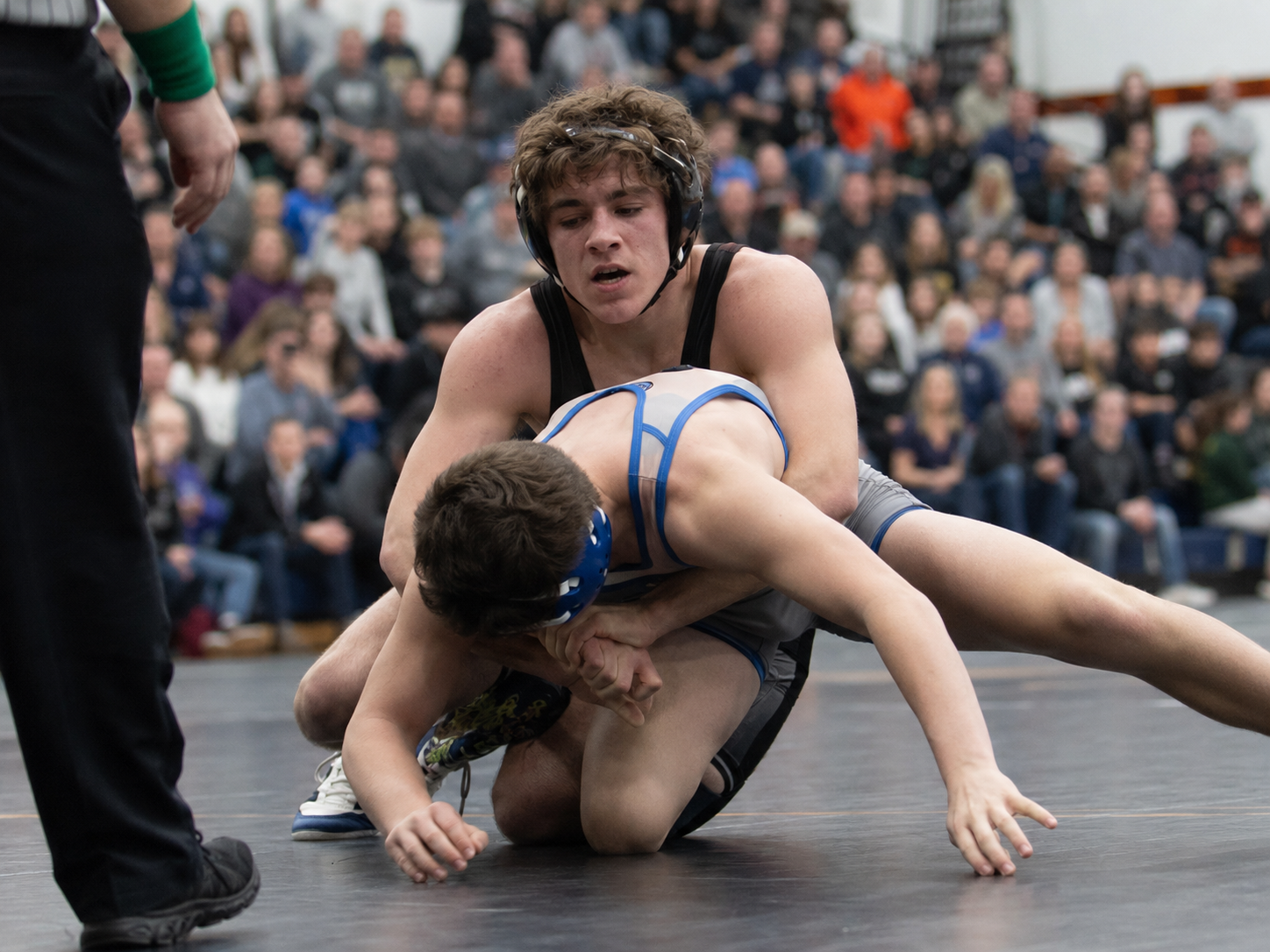 High school wrestler in black singlet pins opponent to the mat during an intense wrestling match.