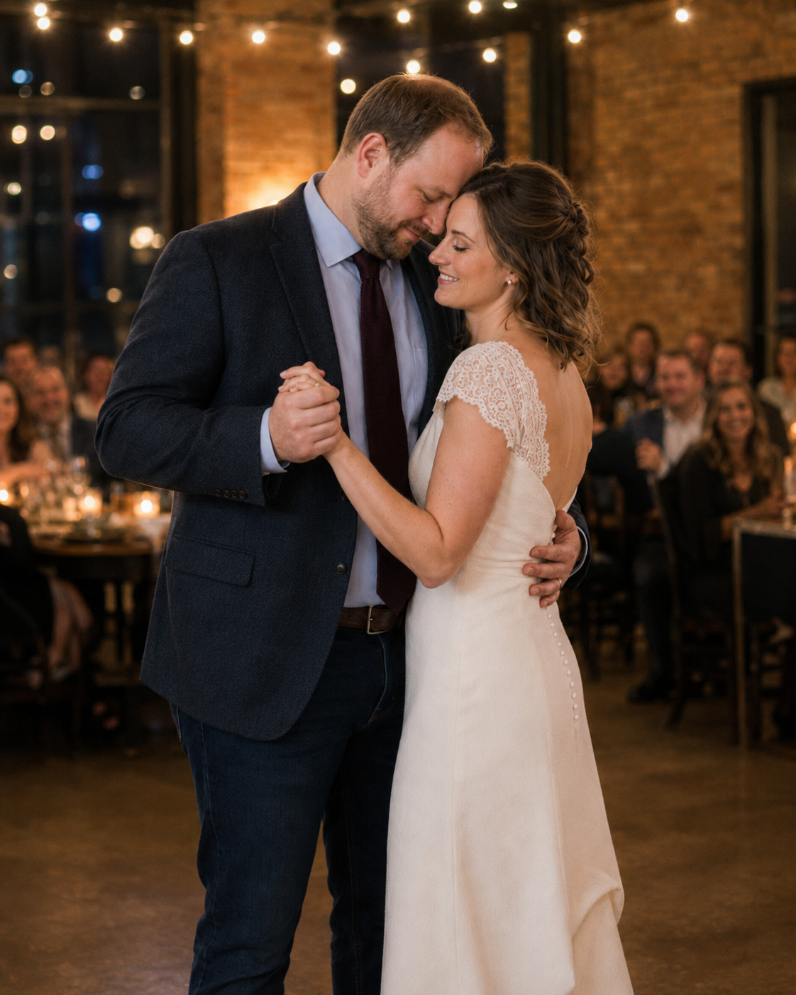 A bride and groom share their first dance at a romantic candlelit wedding reception with string lights.