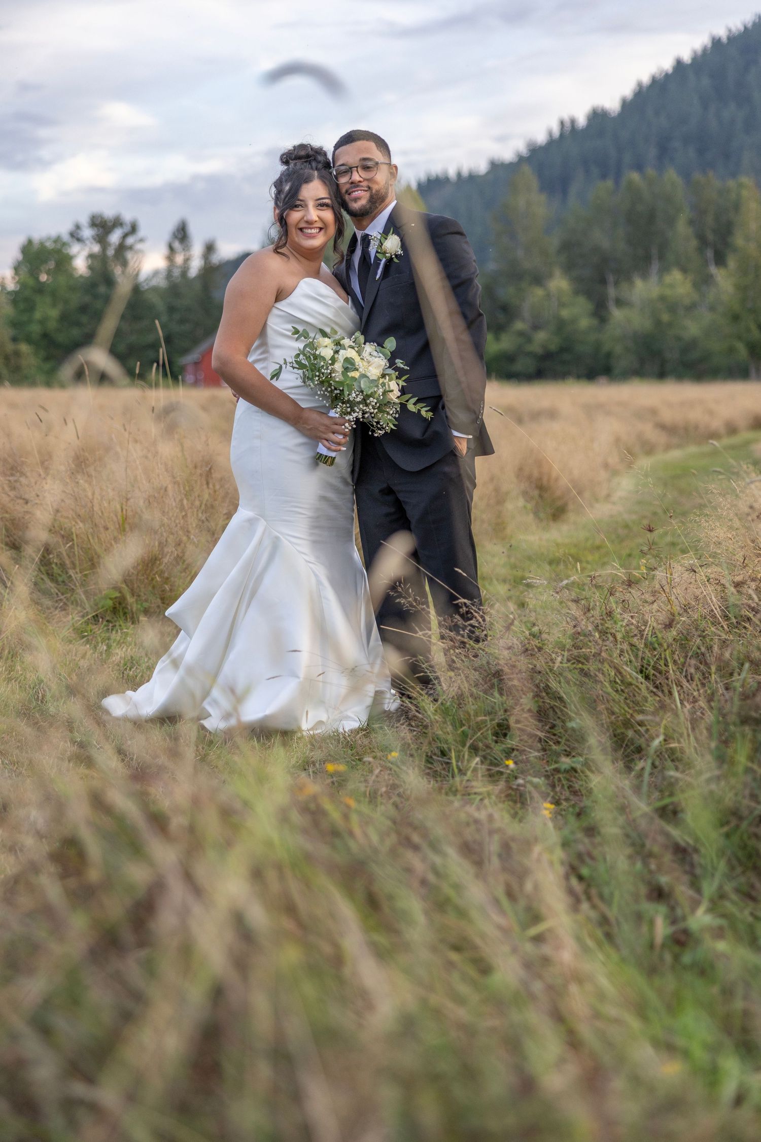 A couple in wedding attire shares a romantic moment together in a scenic field with mountains in the background.