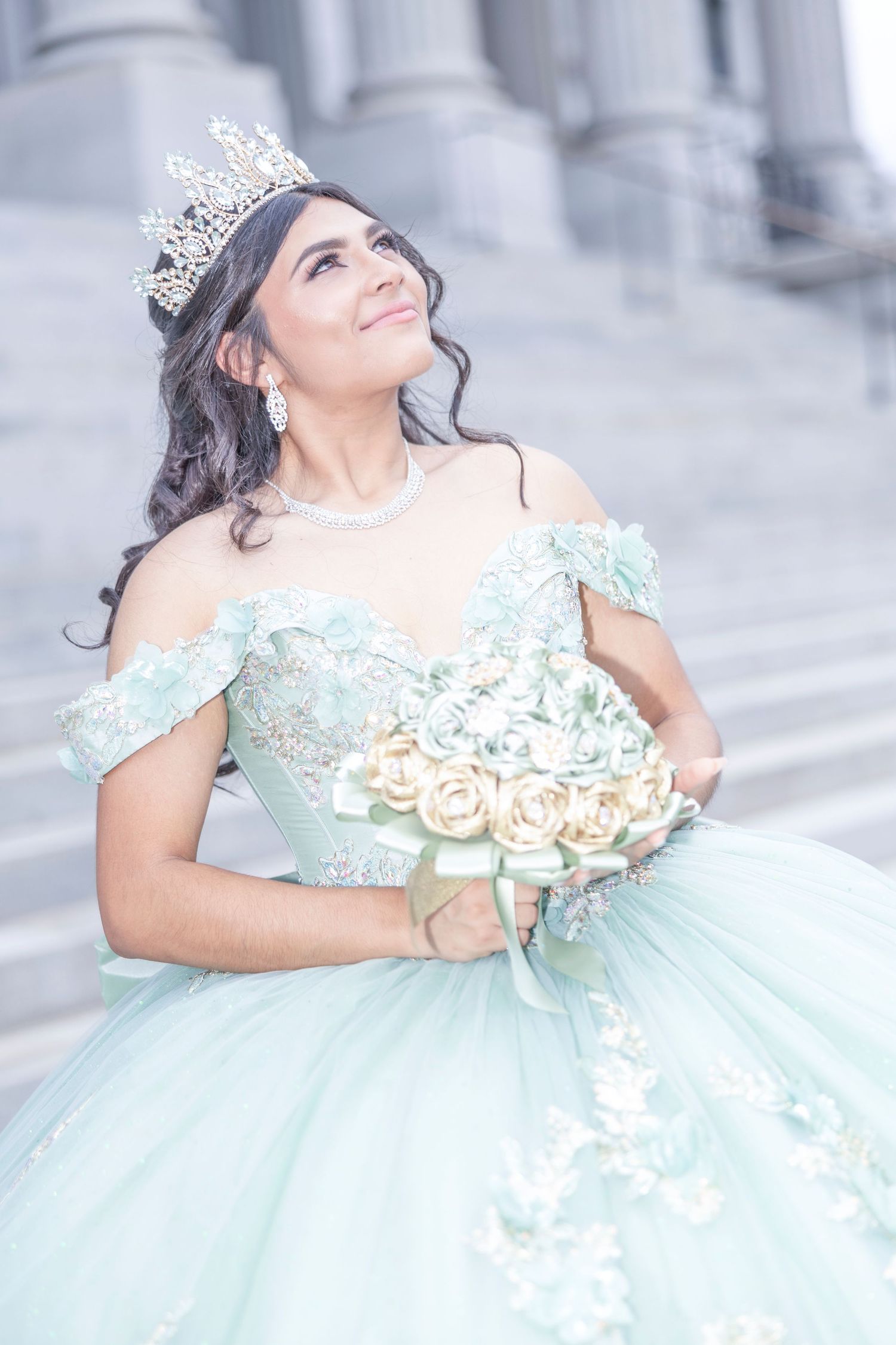 A quinceañera dress in mint green tulle with floral appliques is showcased in a dreamy outdoor photoshoot.