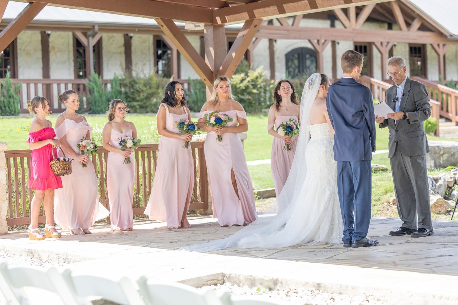 A wedding party stands together on a rustic wooden deck during an outdoor ceremony.