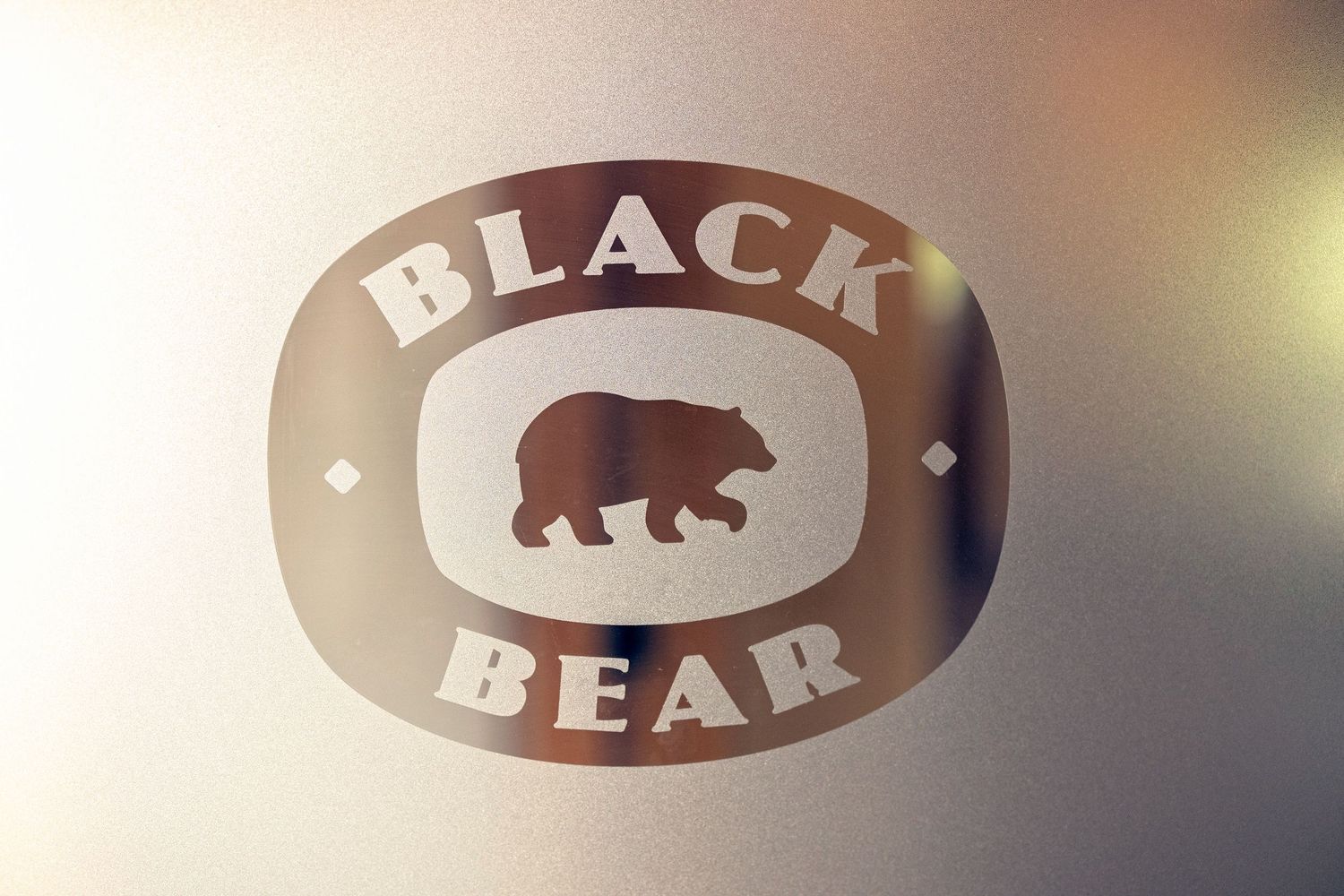 A brown and white oval logo design featuring a silhouette of a black bear against a blurred background.