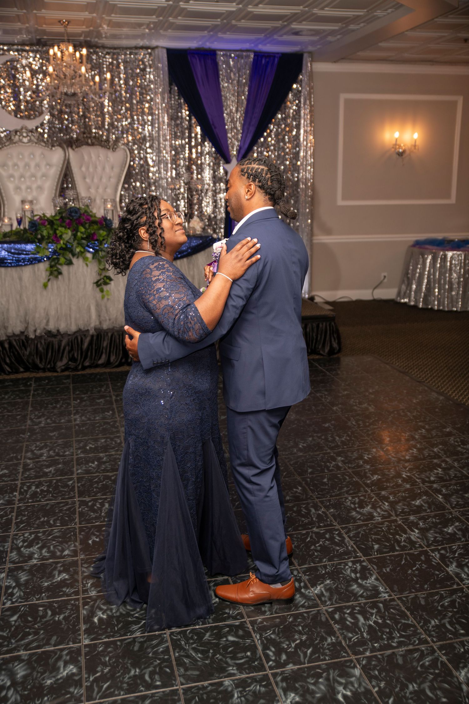 Two people share a dance on a shiny marble floor under sparkling decorations at an elegant event venue.