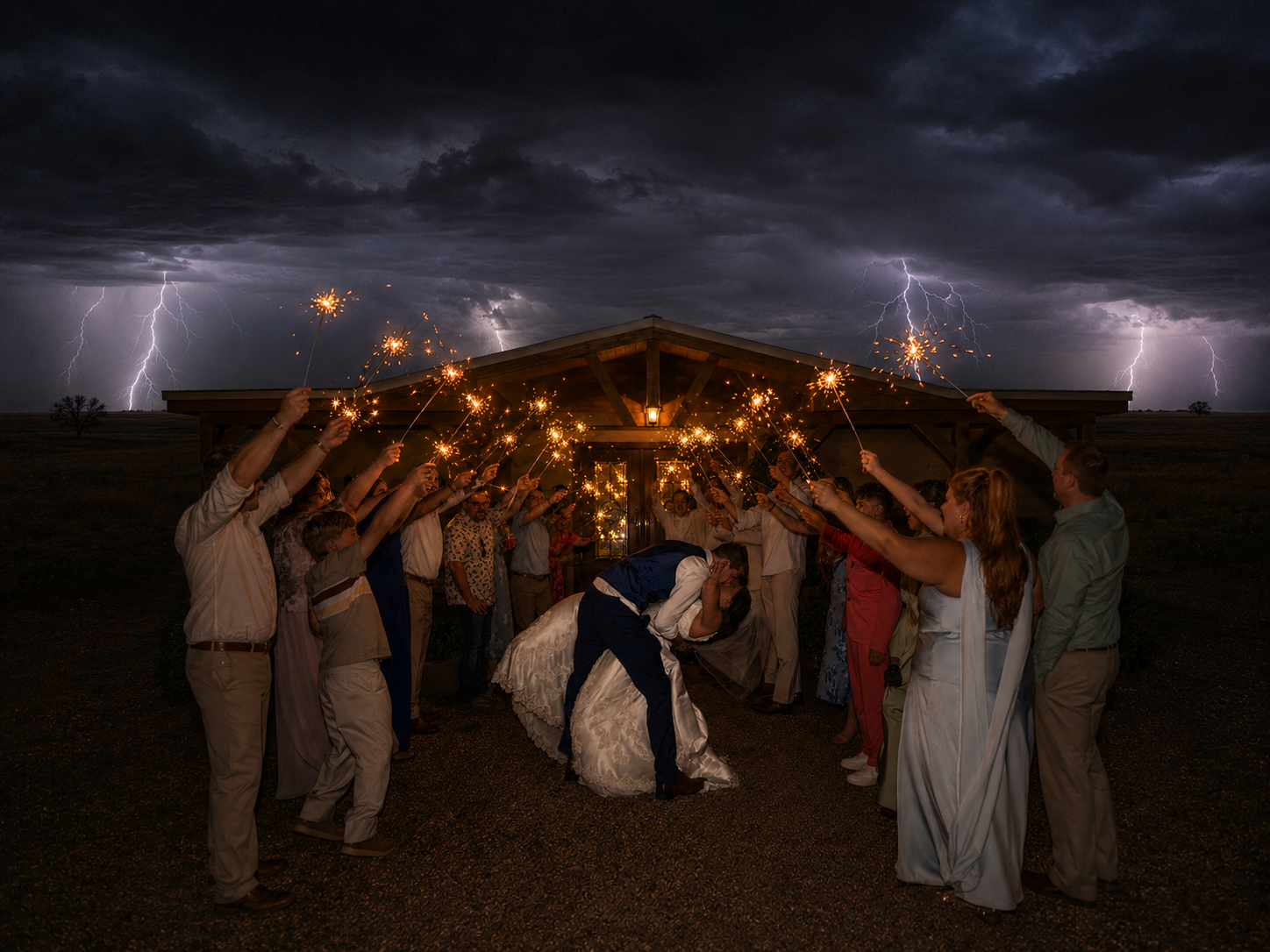 Wedding couple kissing under sparkler tunnel with dramatic lightning storm in background at rustic outdoor venue.
