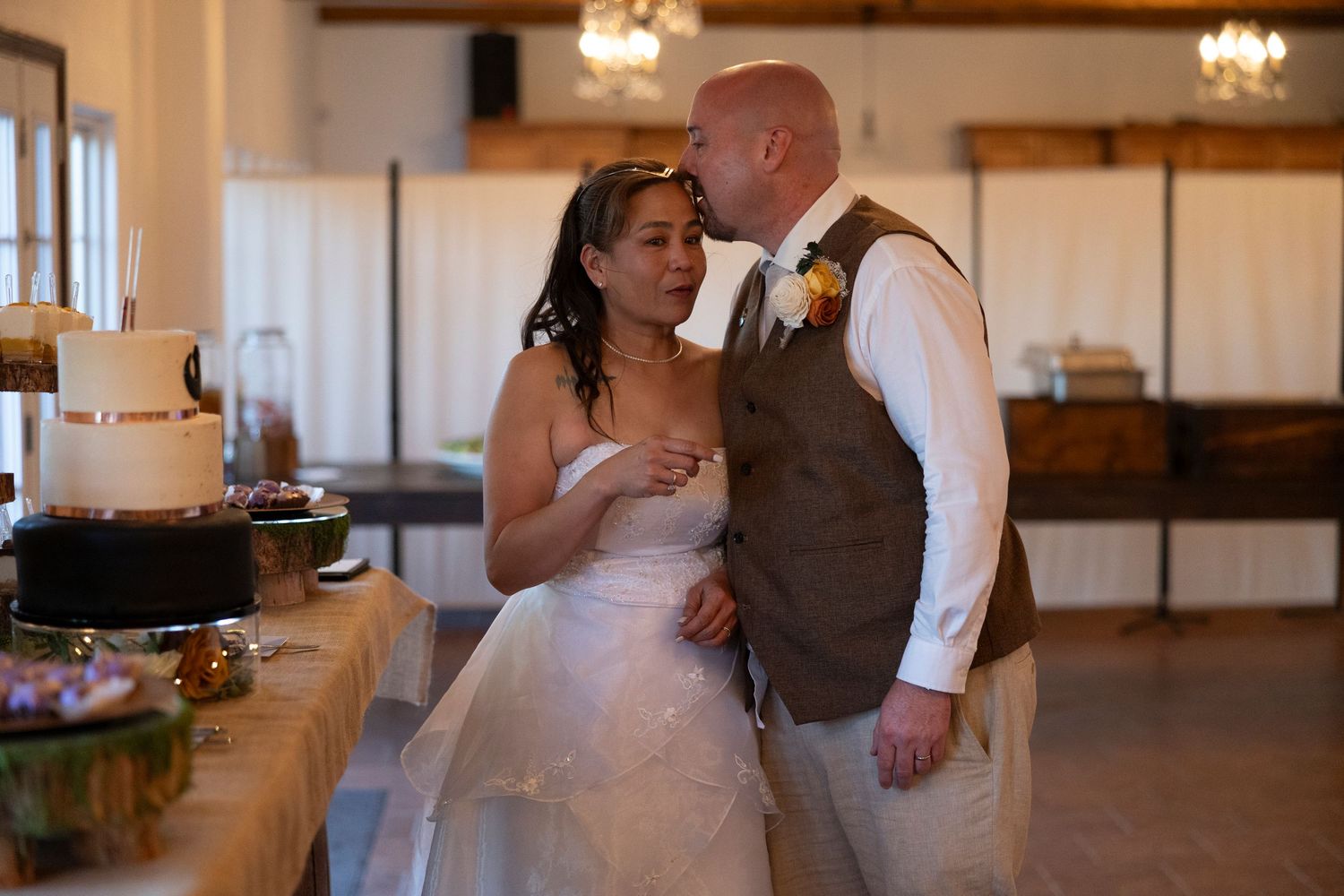 Bride and groom share a tender kiss during wedding reception cake cutting ceremony in elegant venue.