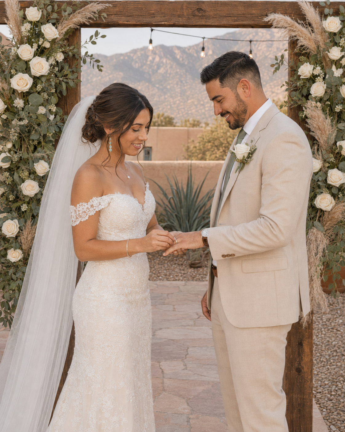 Bride and groom exchanging rings under a floral arch with mountain backdrop at an outdoor desert wedding ceremony.