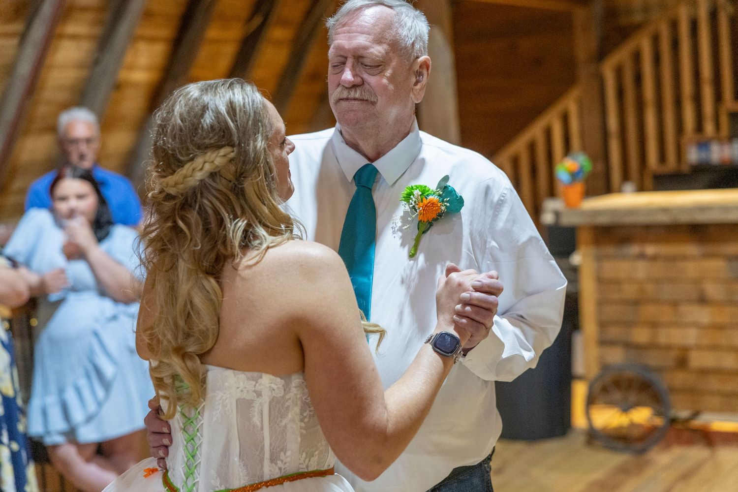 Father and bride share an emotional first dance at a rustic wedding venue with wooden decor.