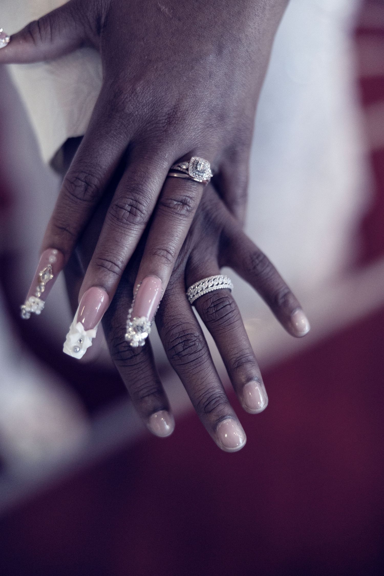 Close-up of two hands adorned with diamond engagement rings and decorated acrylic nails, celebrating a wedding union.