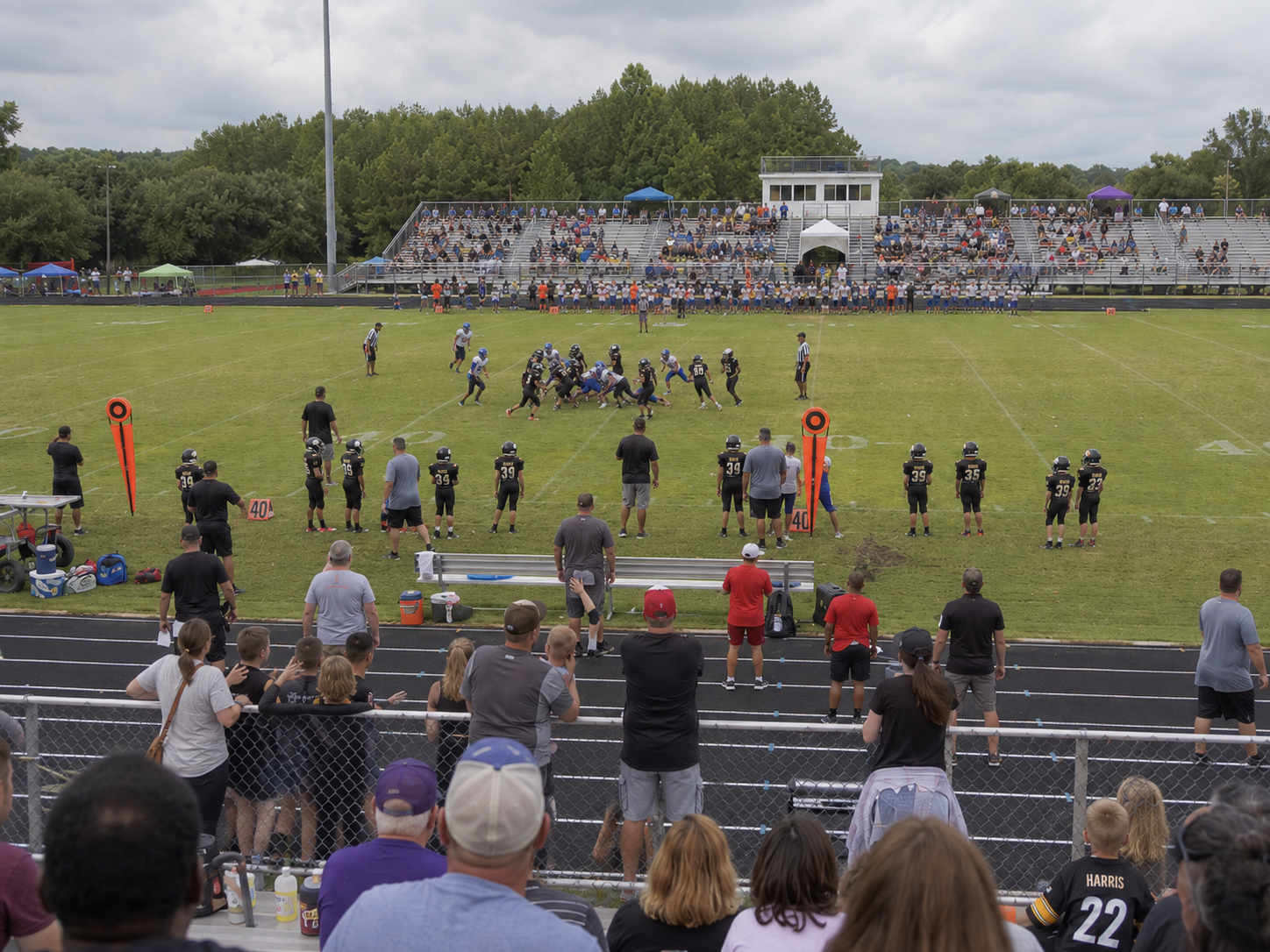 Spectators watch a youth football game from the stands at a well-attended outdoor stadium event.