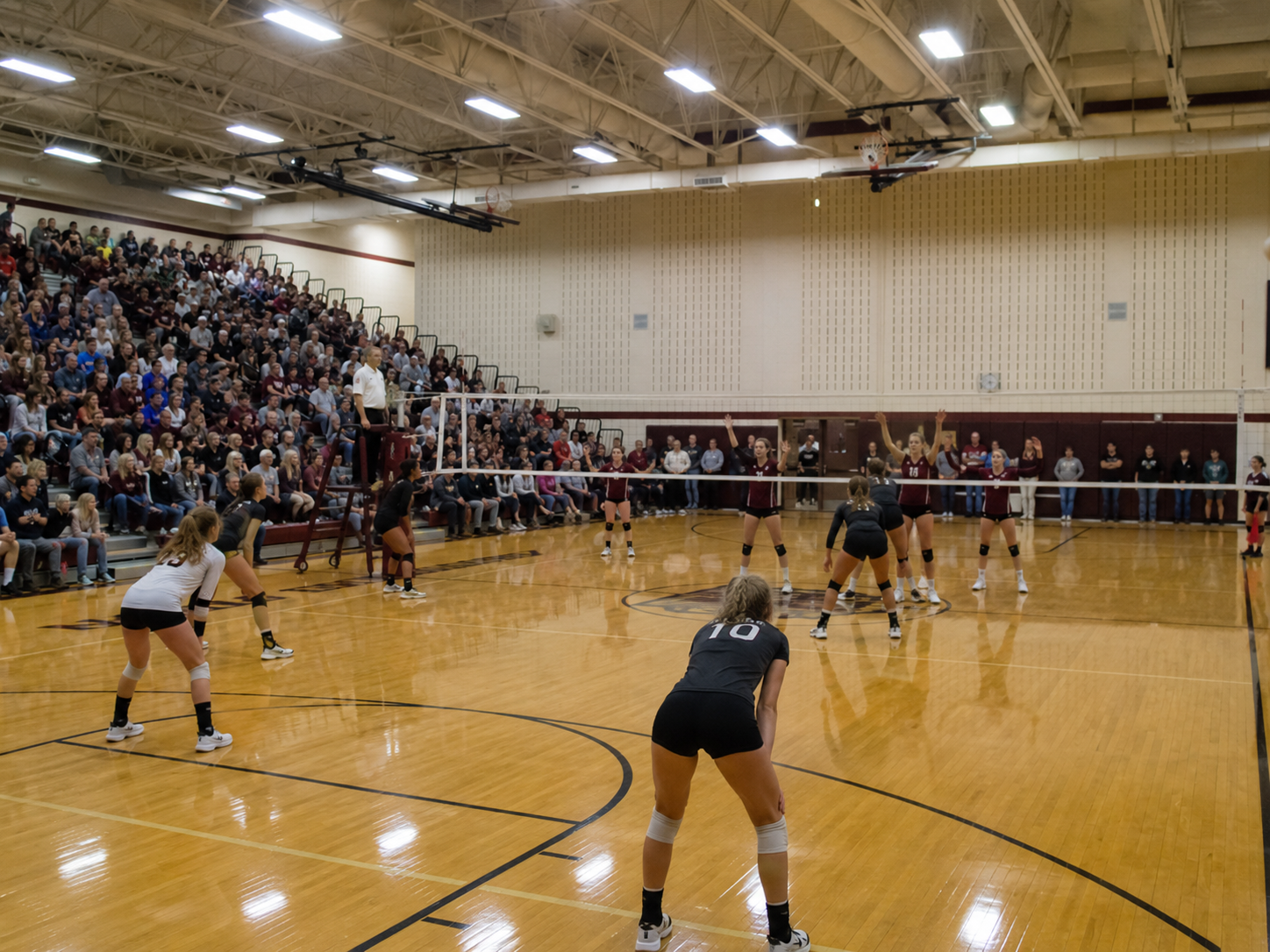High school volleyball players compete in a packed gymnasium during an intense evening match.