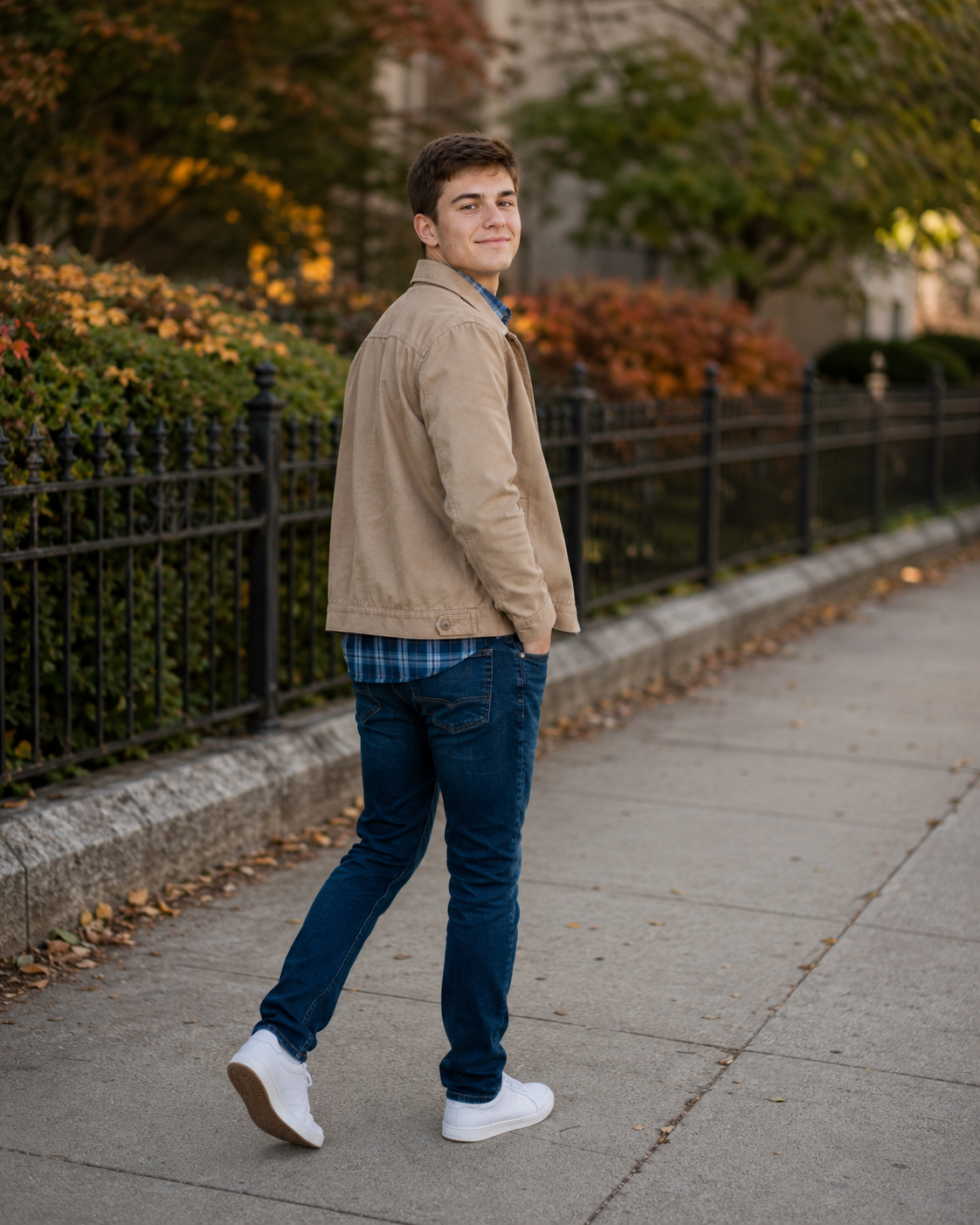 Young man in tan jacket and jeans walking on urban sidewalk in autumn.