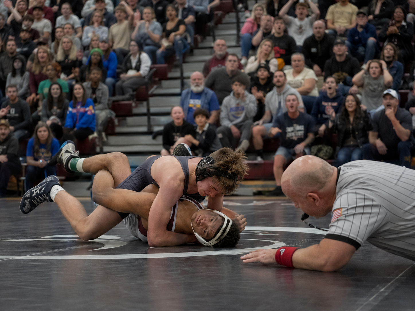 Wrestler pins opponent to mat as referee watches closely during competitive wrestling match.