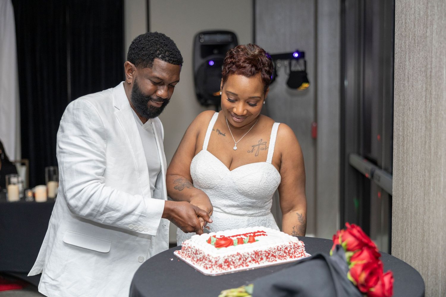 A couple in white attire cuts their wedding cake together during their reception celebration.