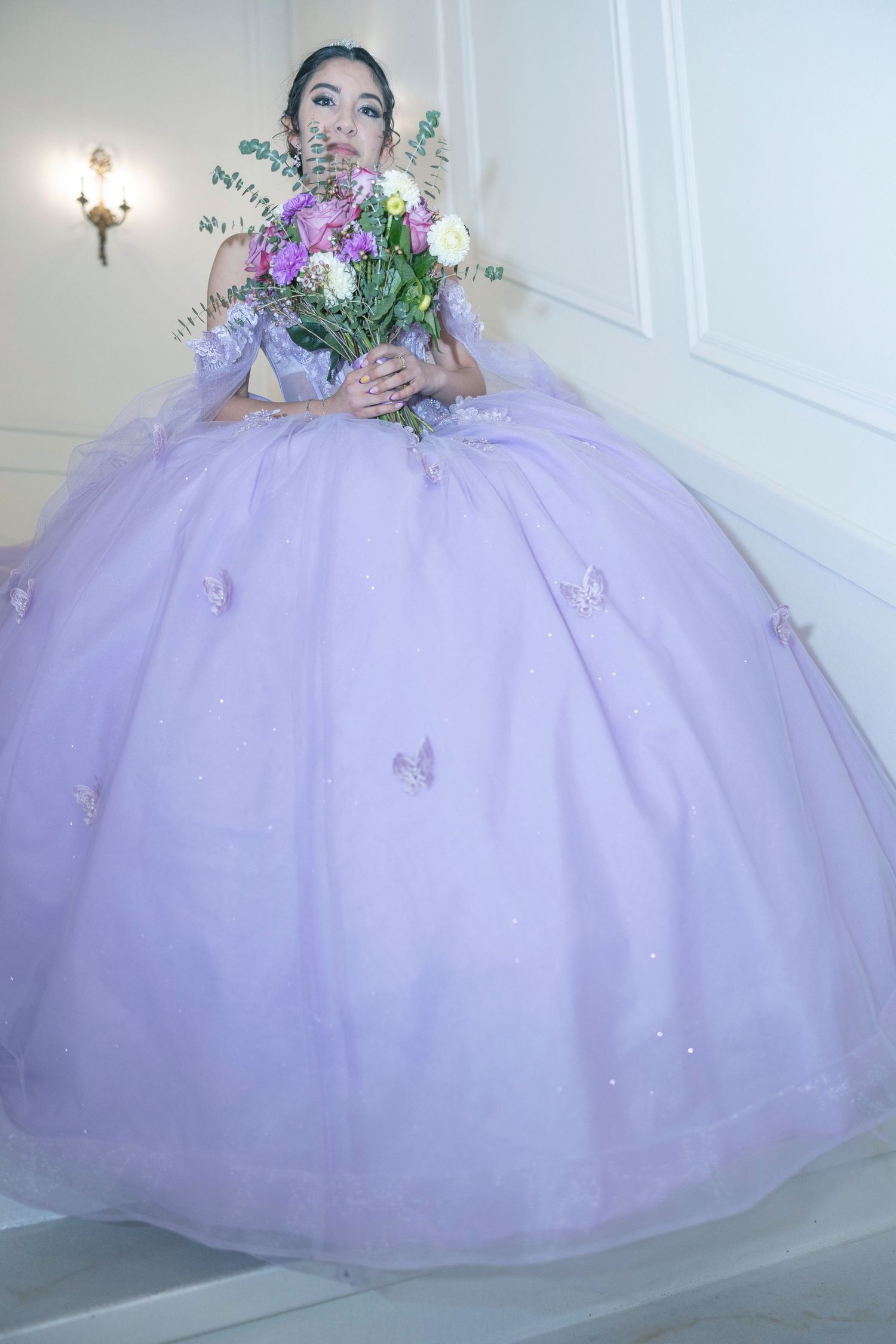 A lavender purple ball gown with tulle skirt and floral details photographed in a bright white room.