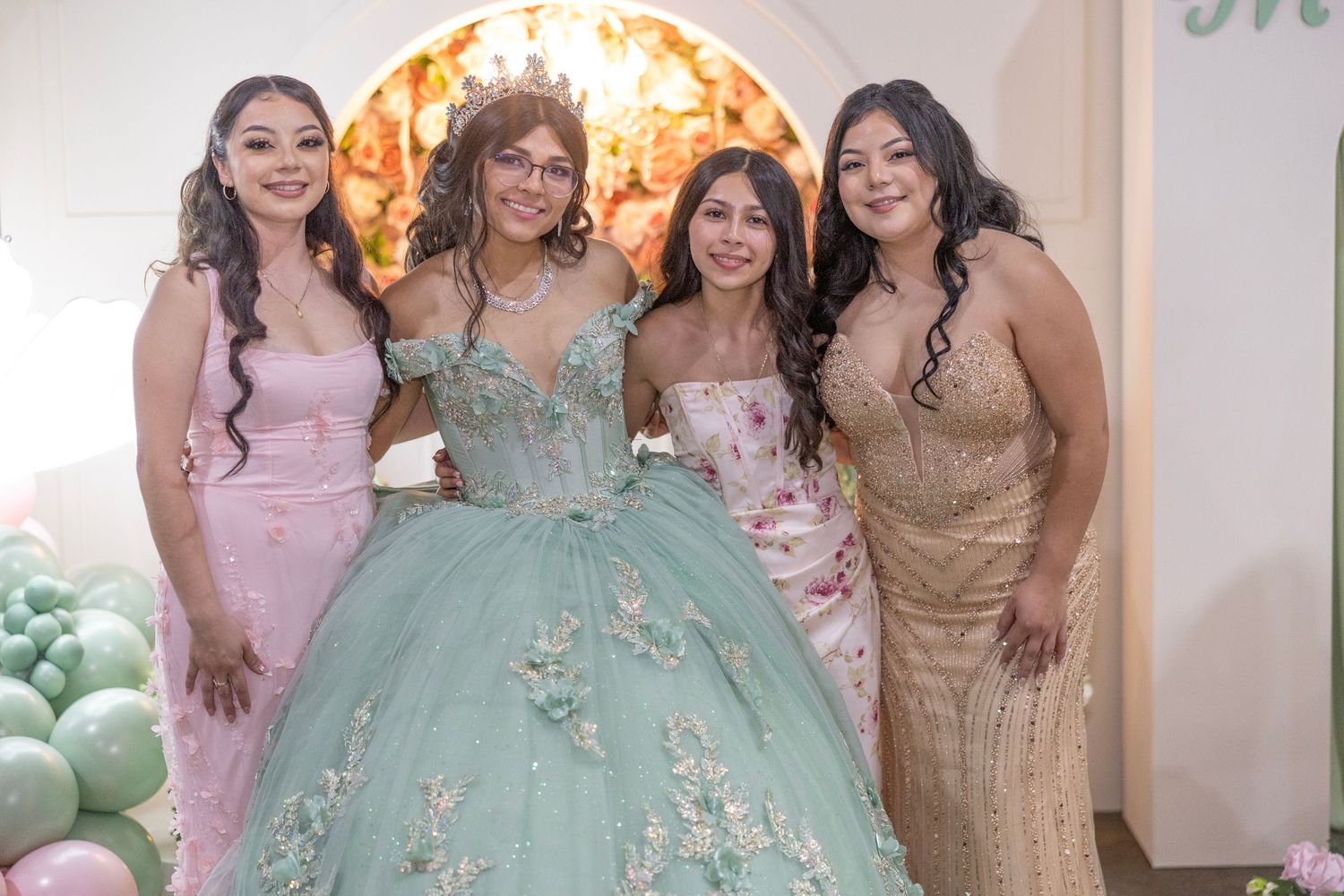 A group poses together at a formal event, with the central figure wearing a mint green ball gown with floral details.