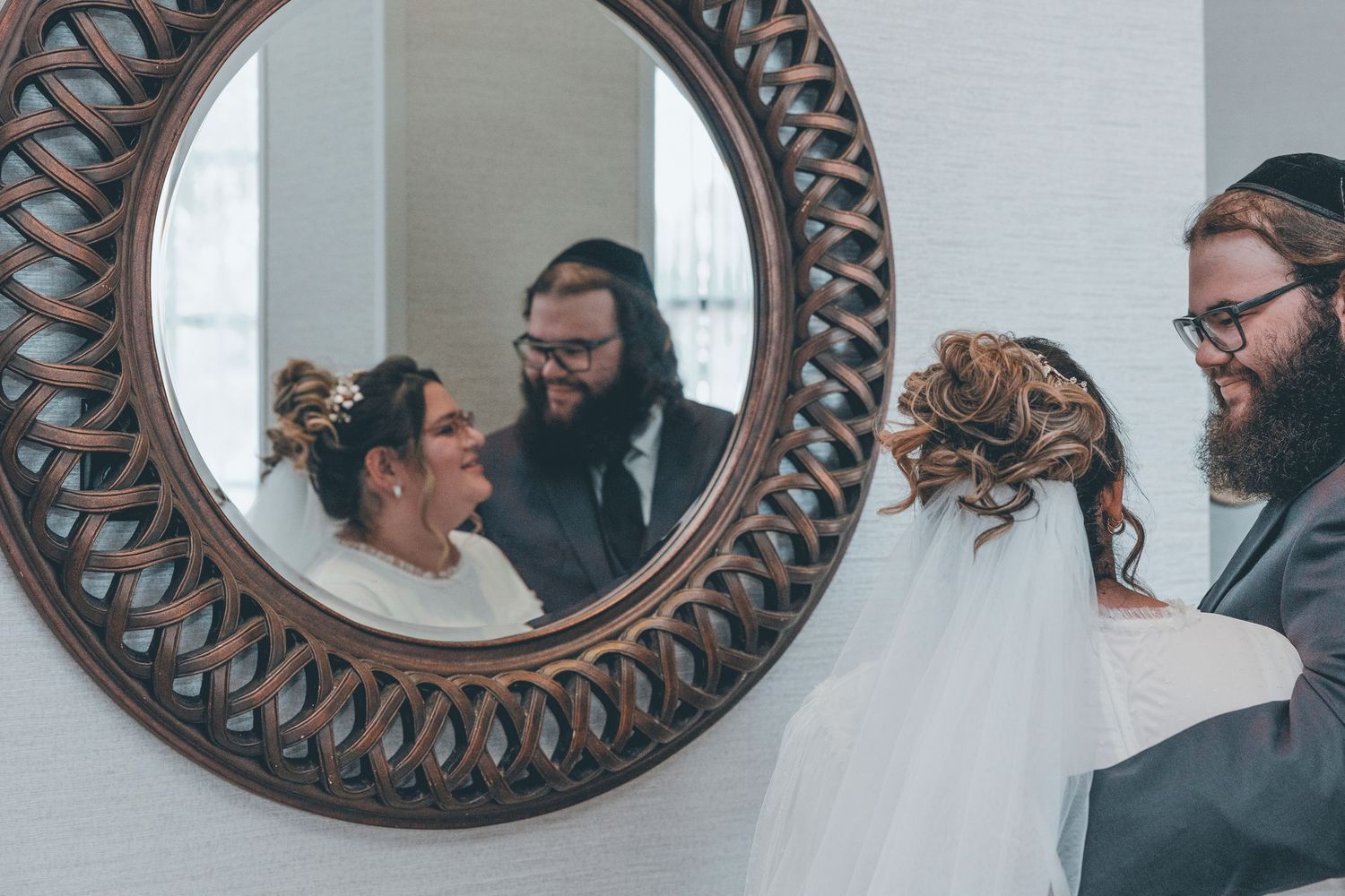A row of decorative round mirrors with dark ornate frames hang on a white wall, reflecting people in a room.