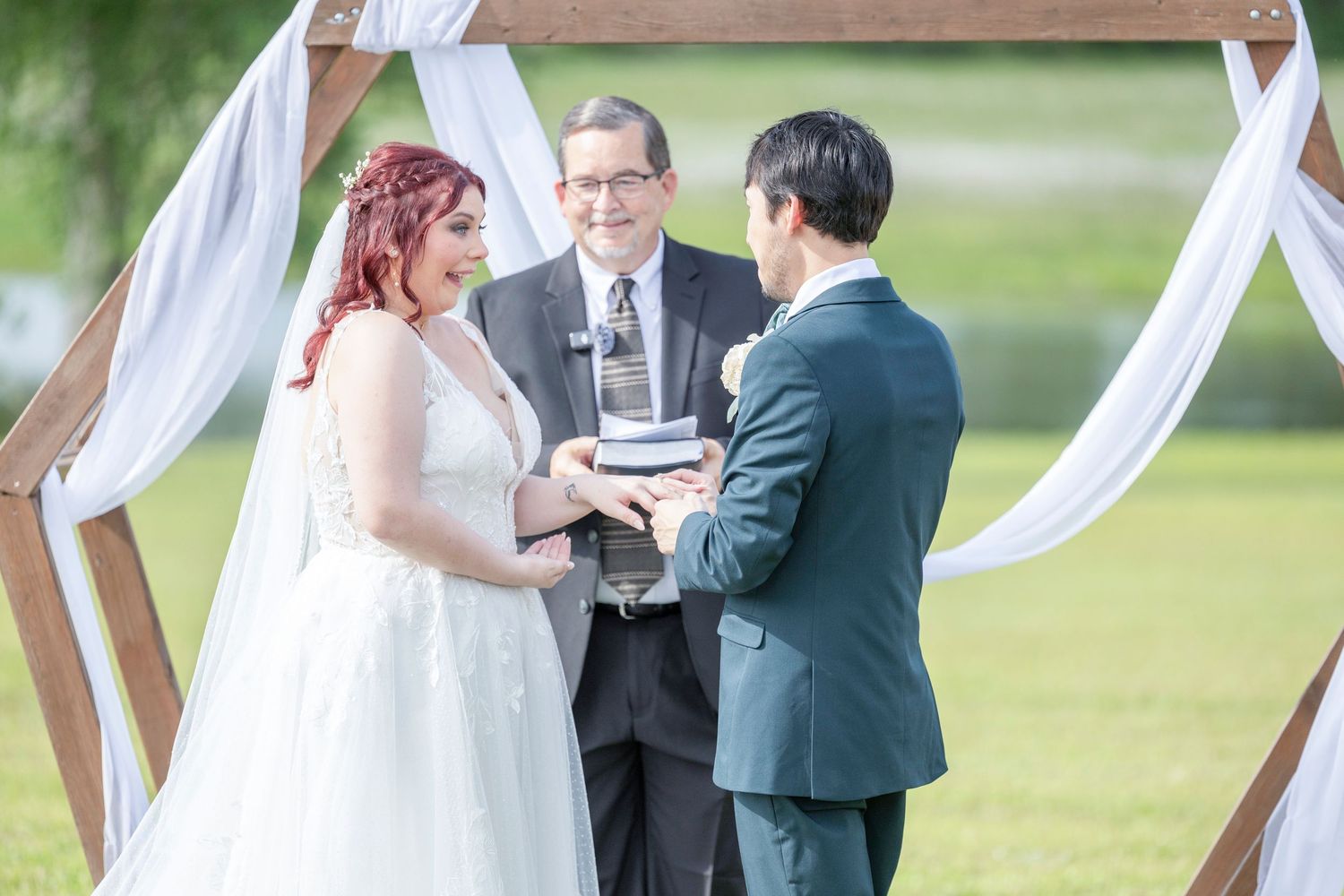 A couple exchanges vows during an outdoor wedding ceremony under white fabric draping.