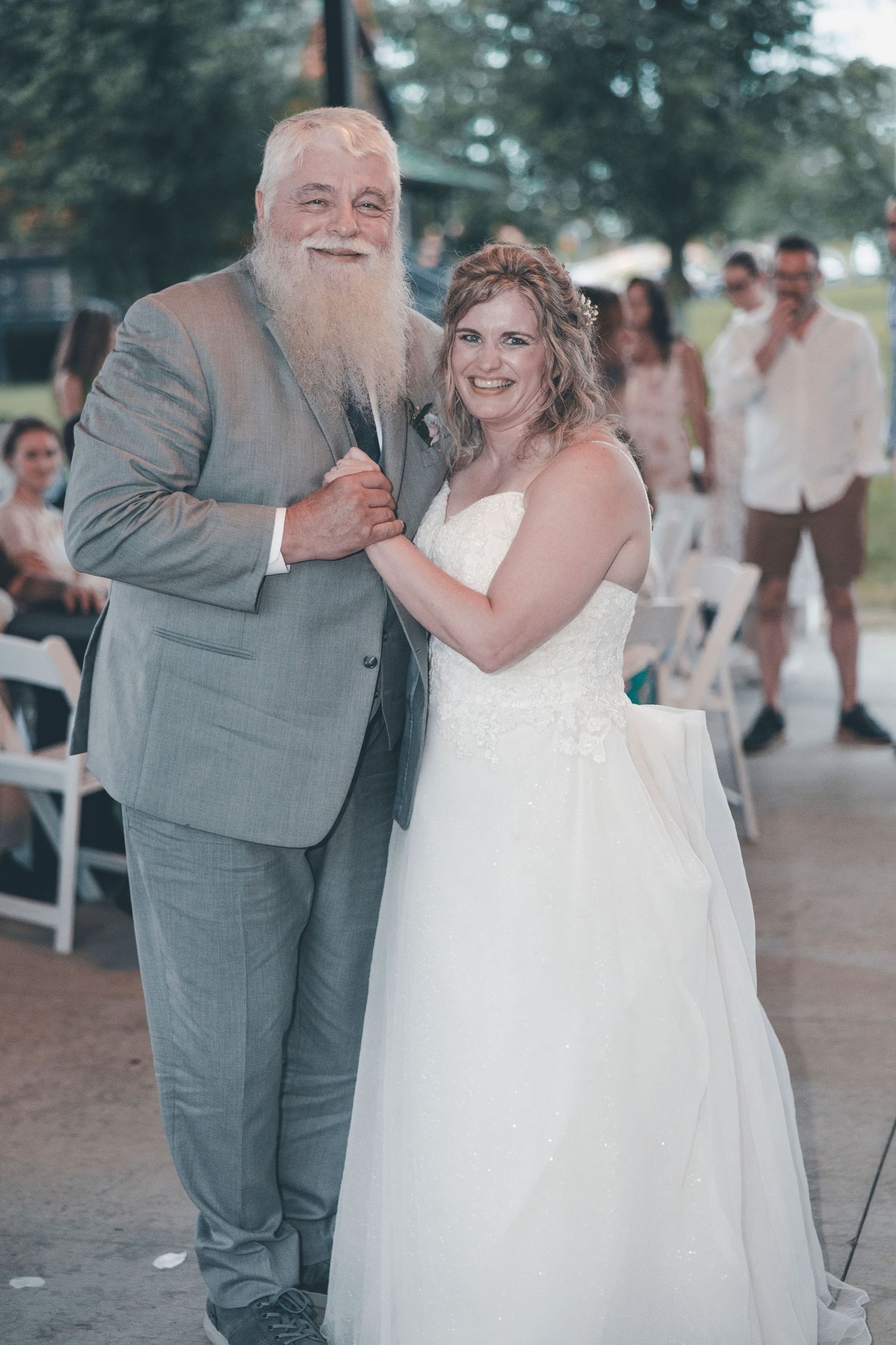 Bride and groom share joyful laughter while dancing together at an outdoor wedding reception.