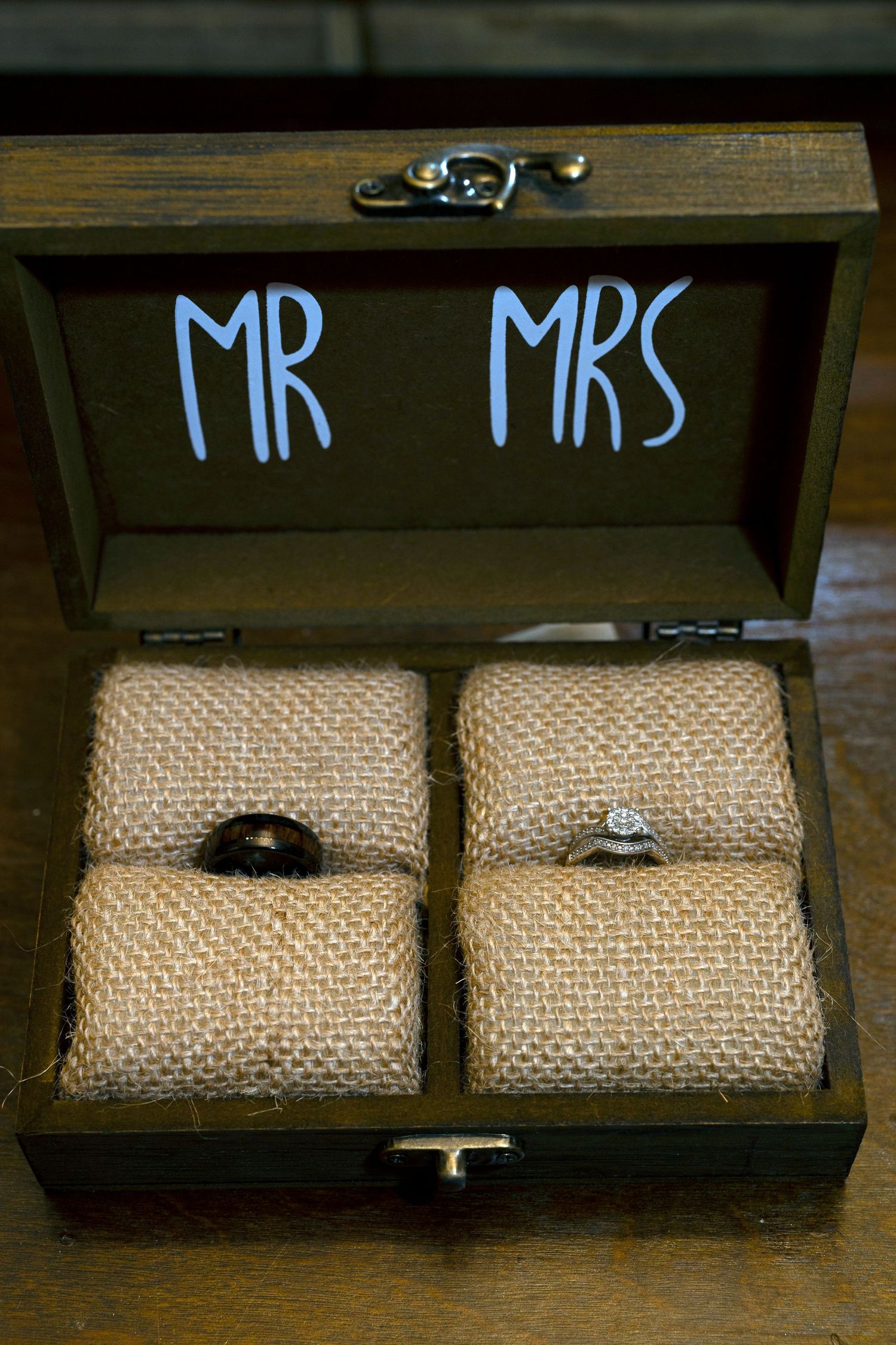 Wedding rings nestled on burlap cushions inside a rustic wooden box with 'MR MRS' painted on the lid.