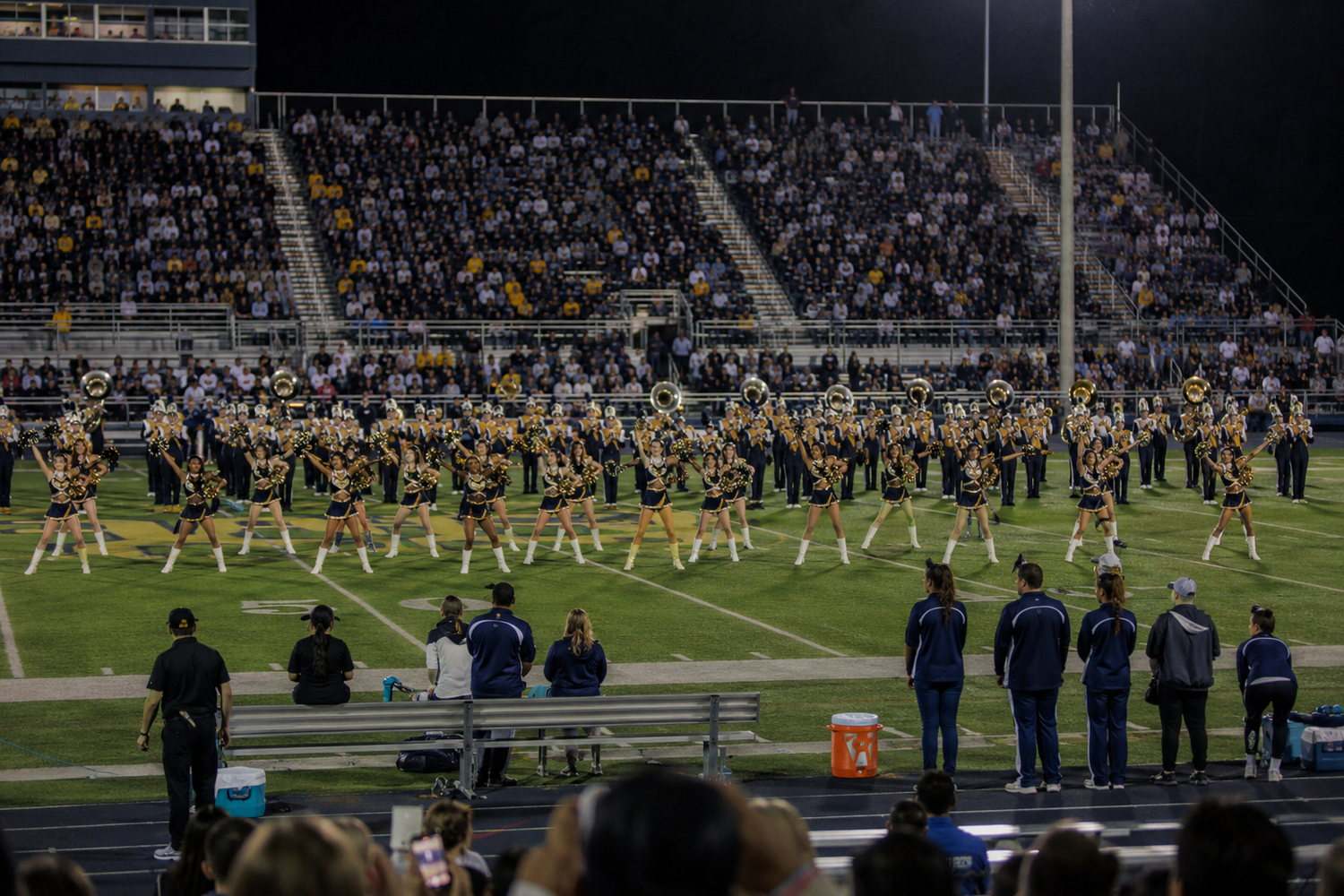 Marching band and dance team perform on football field before a large stadium crowd.