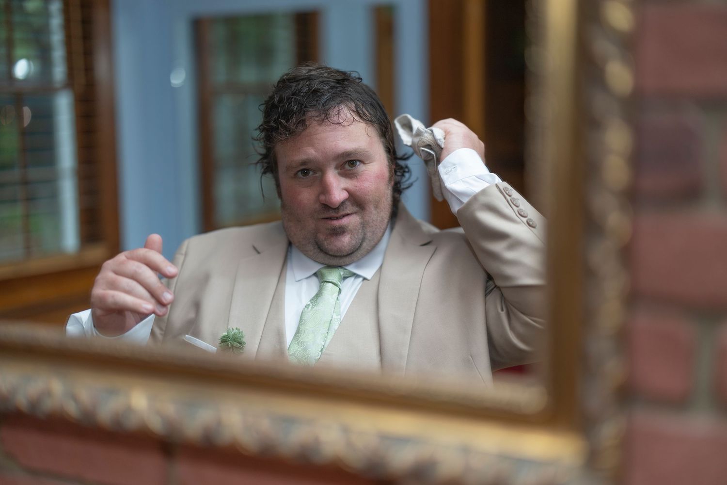 Someone in a beige suit jacket holds up a microphone while making an expression through a window reflection.