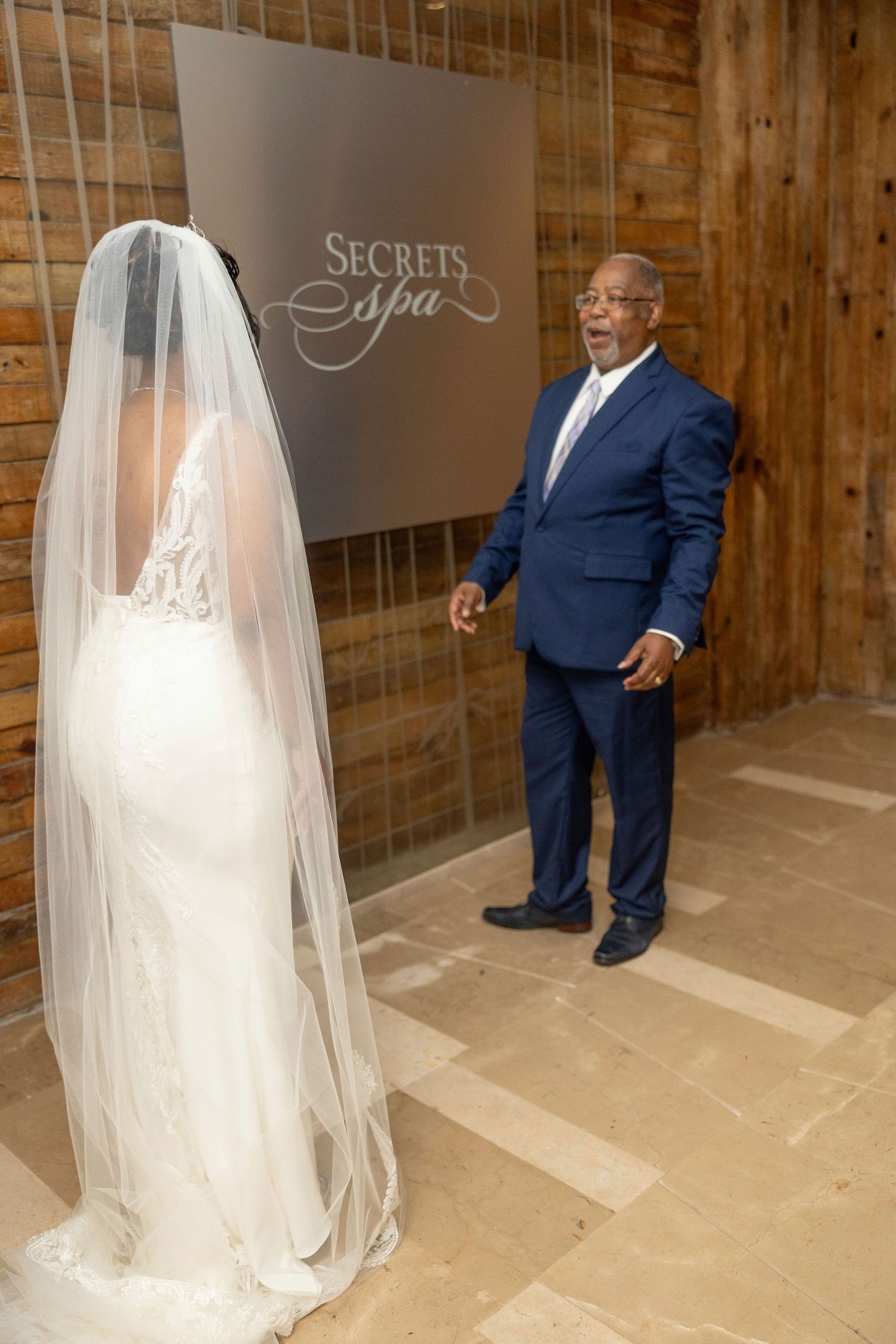 A wedding scene showing a flowing white veil and navy suit in a rustic wooden barn venue.