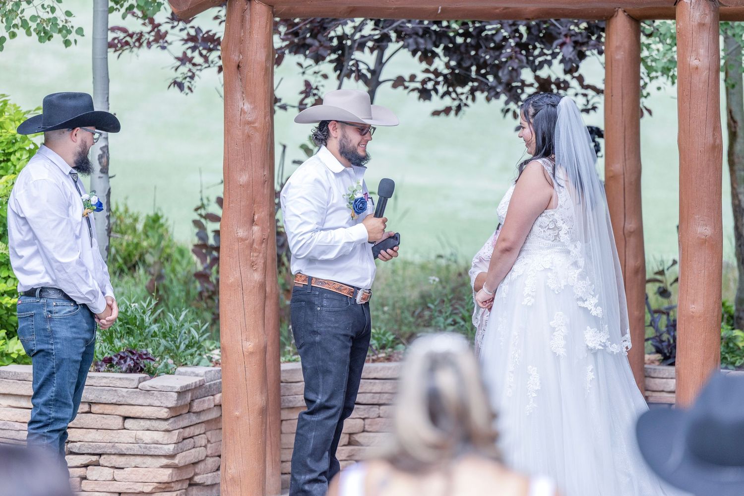 A couple shares a romantic moment under wooden beams during an outdoor wedding ceremony.