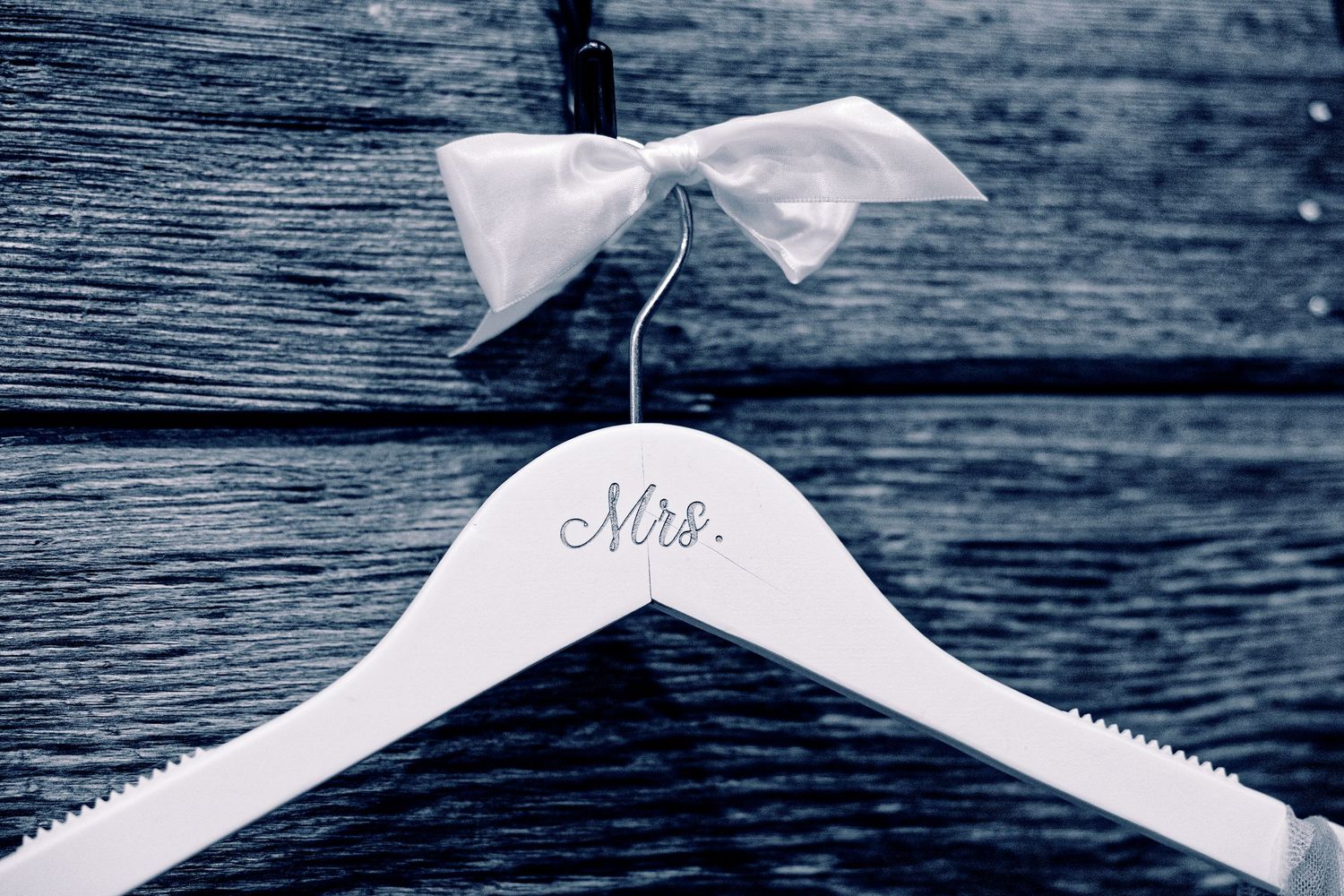 White wedding hanger with Mrs. inscription and white bow on rustic wooden background.