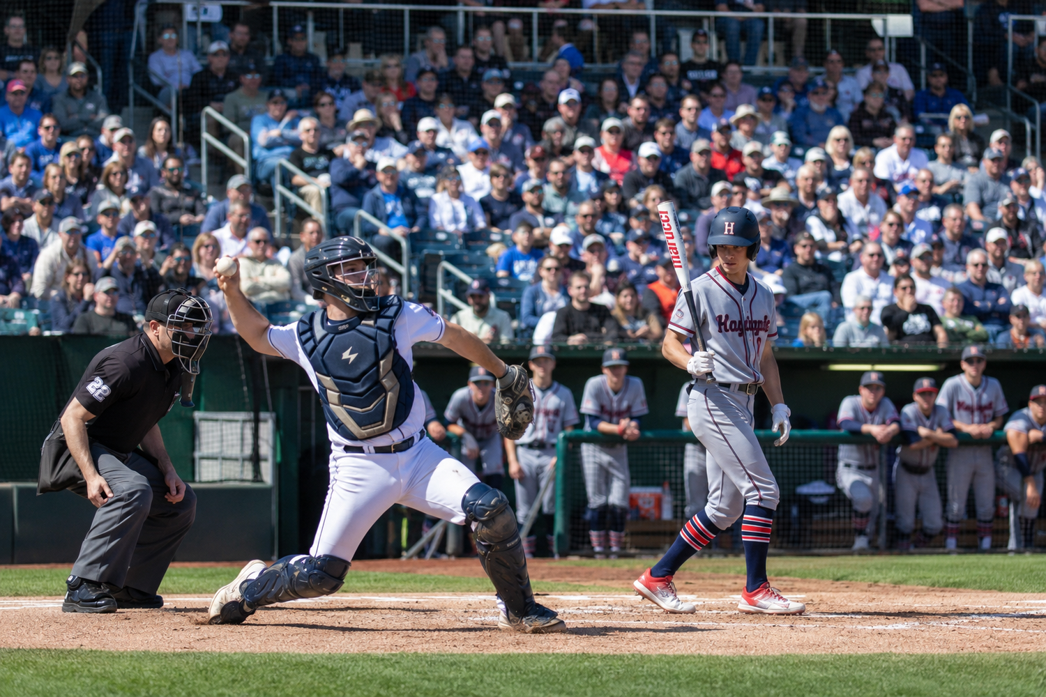Baseball catcher signals after a play at home plate as umpires and opposing runner look on.