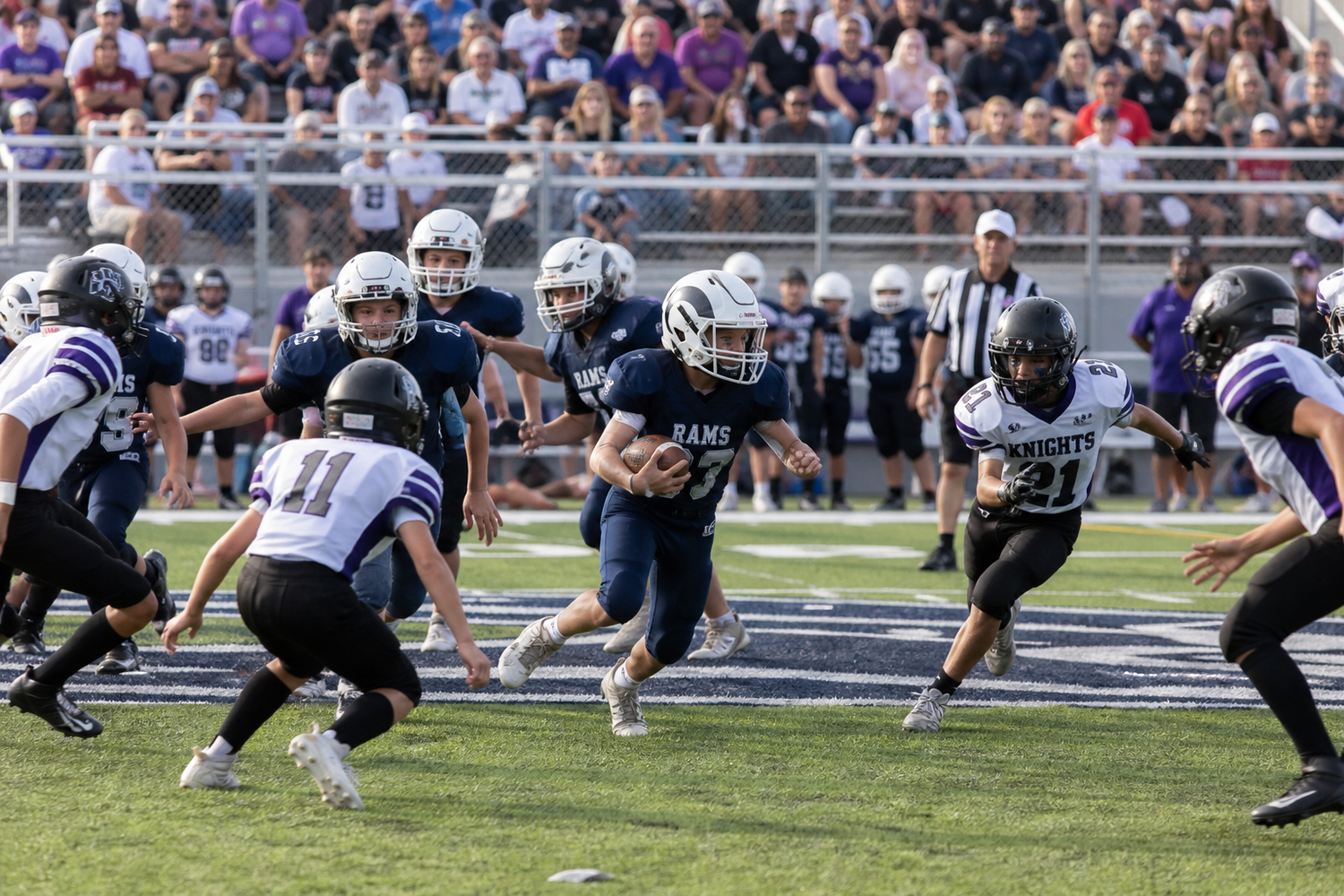 High school football player runs through defenders during a competitive Friday night game under clear skies.