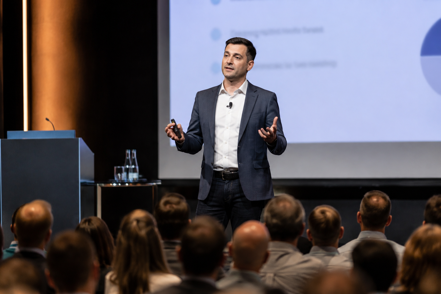 Professional male speaker presents to a business conference audience in a modern event venue.