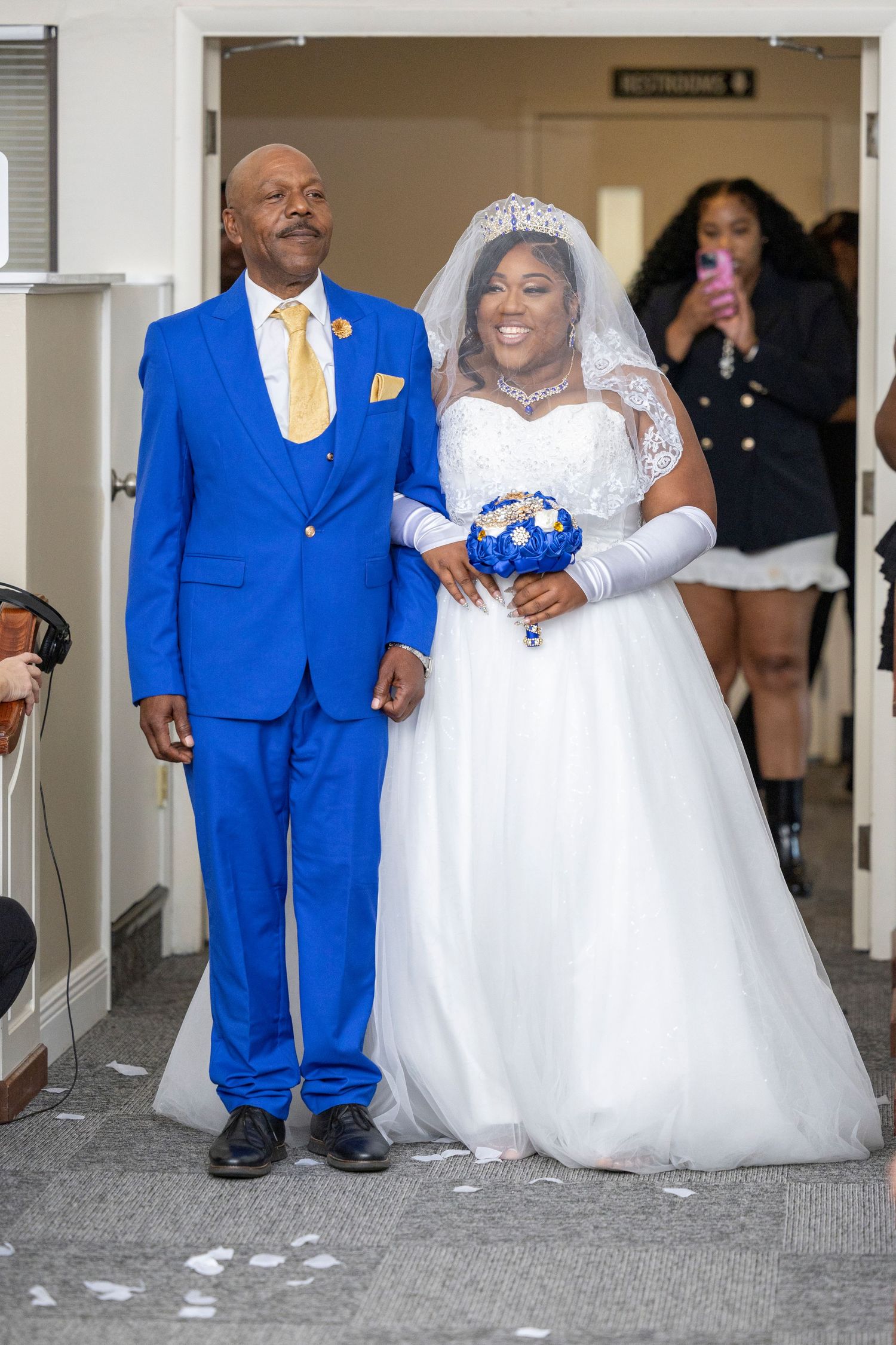 Bride in white gown and groom in royal blue suit walking down the aisle at a wedding ceremony.