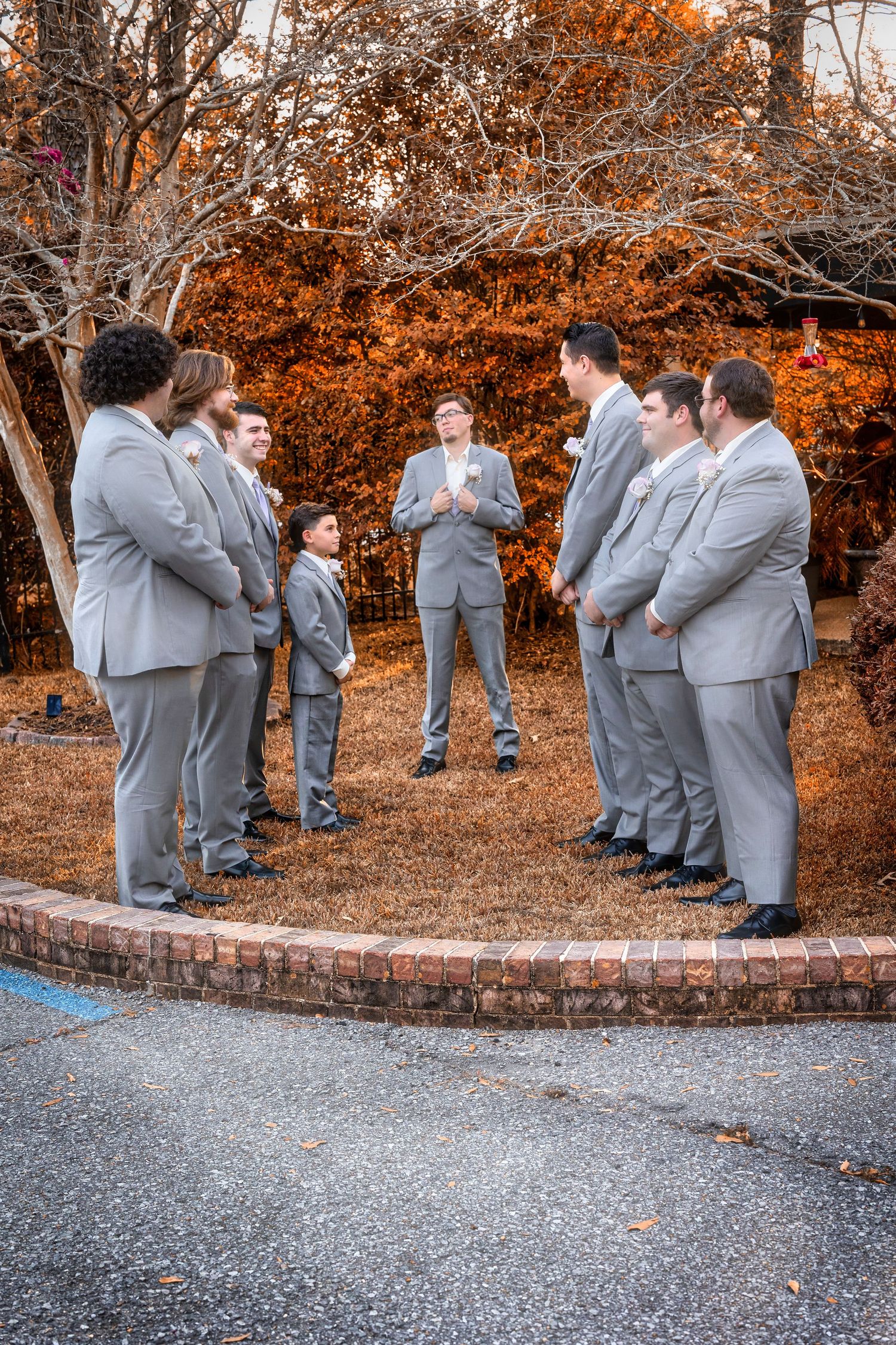 Wedding party in grey suits gathered outdoors during autumn with orange foliage.