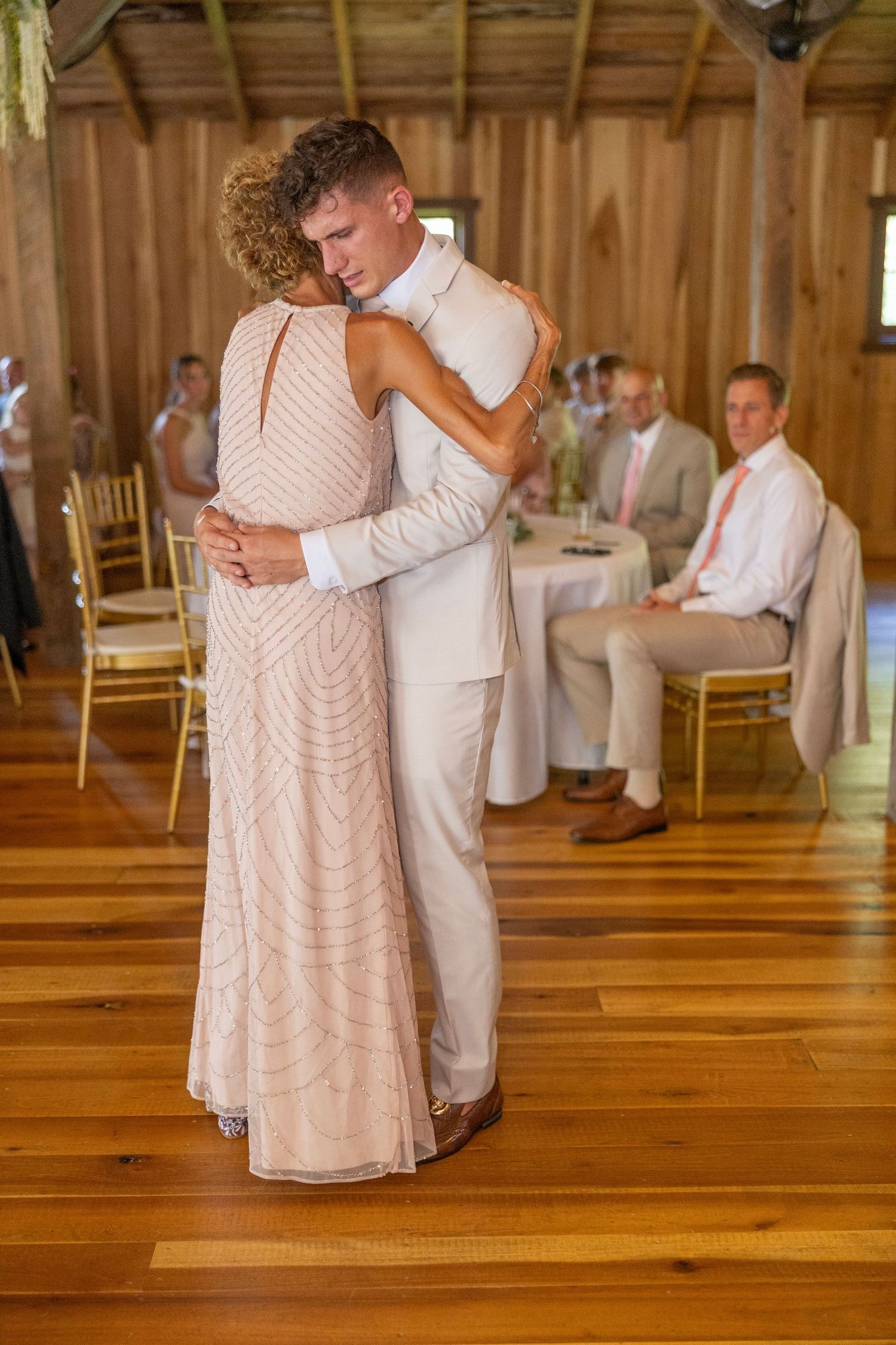 A couple shares a romantic dance on a polished wooden floor at a rustic barn wedding reception.