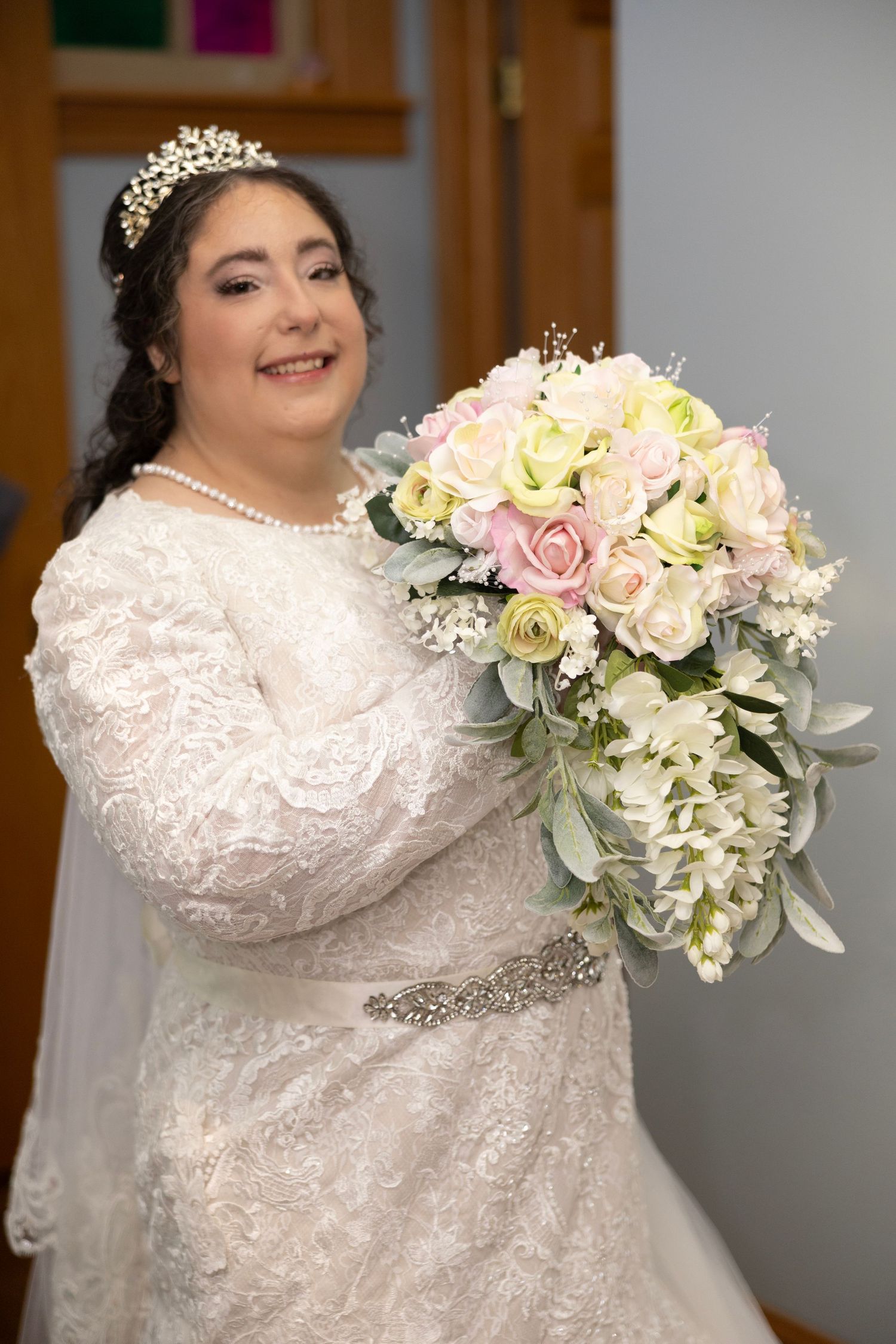 A bride in a white lace wedding dress holds a romantic bouquet of pink and cream roses with eucalyptus.