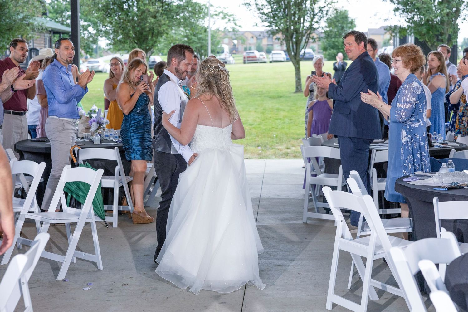 Wedding guests dance and celebrate under a white tent at an outdoor reception venue.
