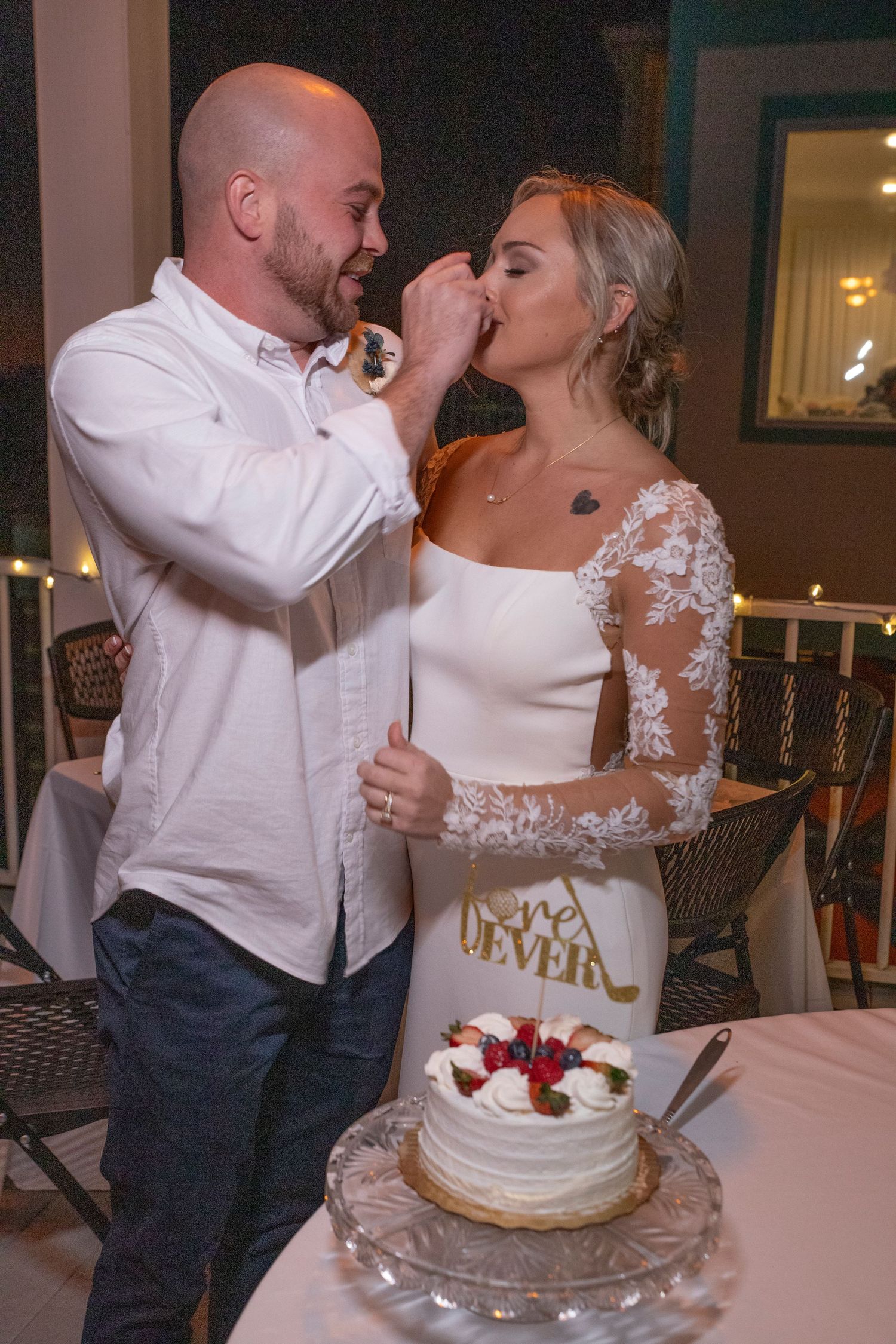Newlyweds share a bite of their white wedding cake topped with fresh berries during reception celebration.