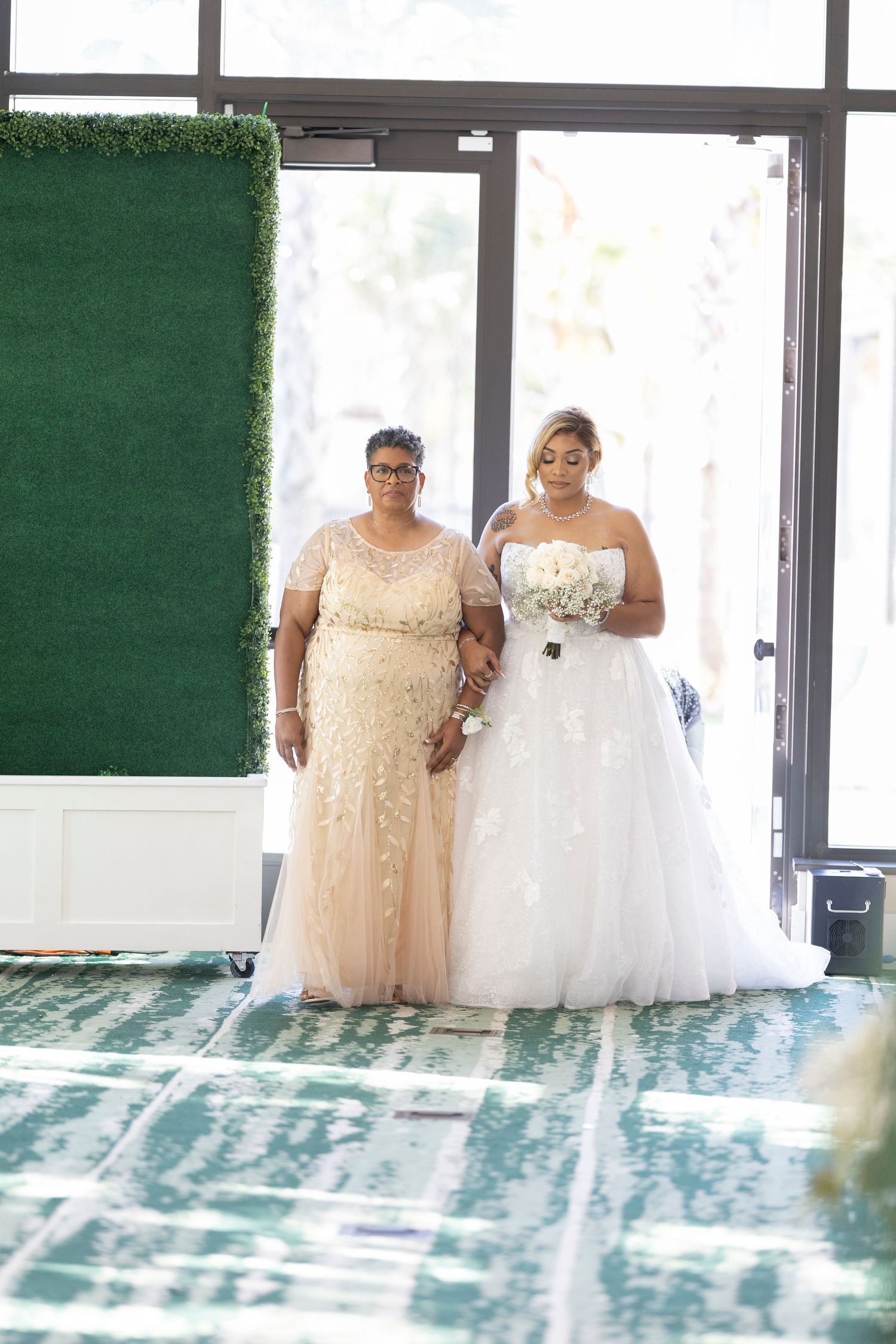 Two people in formal attire pose together at a wedding, wearing a champagne lace gown and white tulle bridal dress.