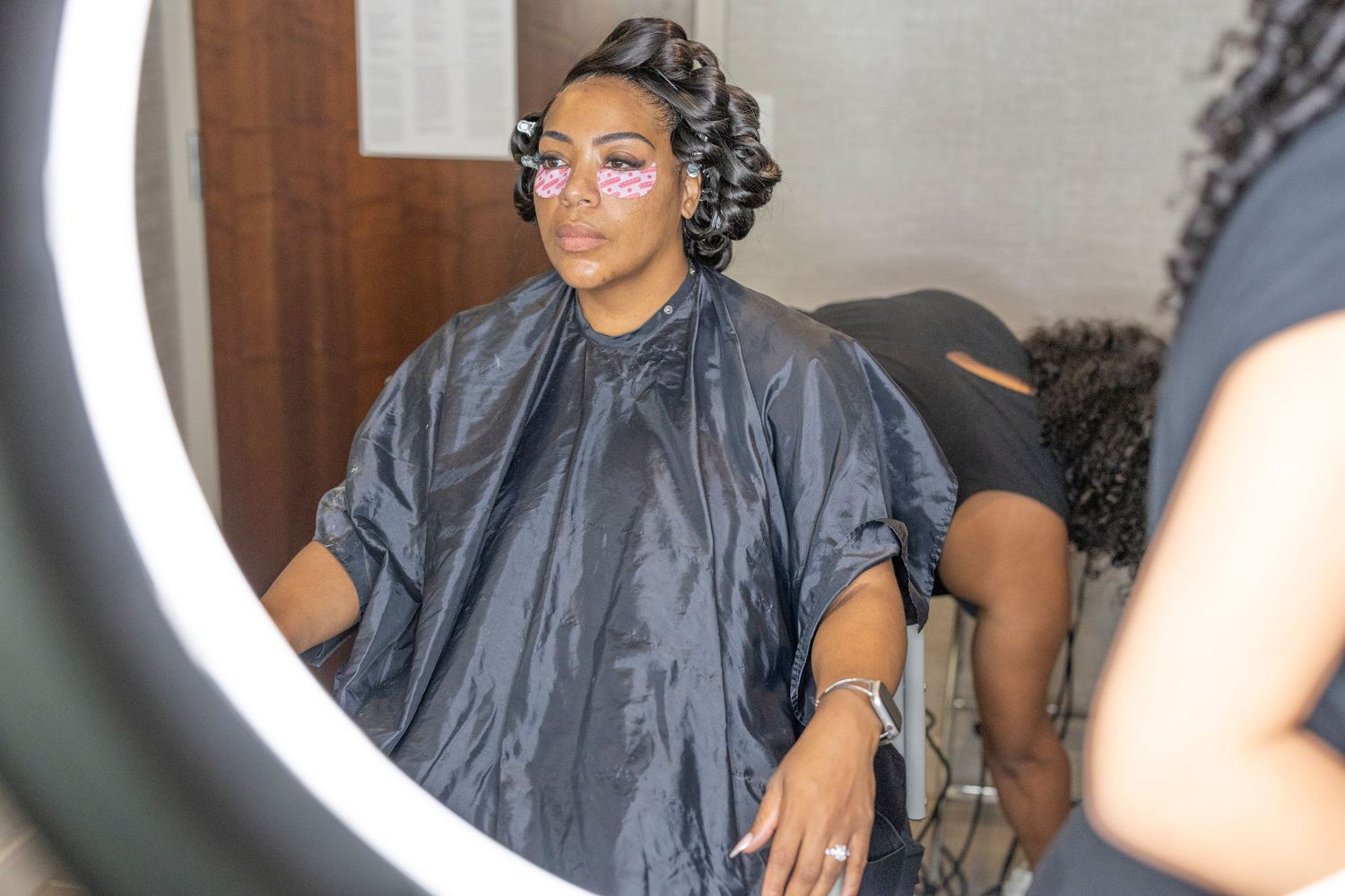 A person wearing a gray salon cape sits in a hairstylist's chair while getting their hair styled.
