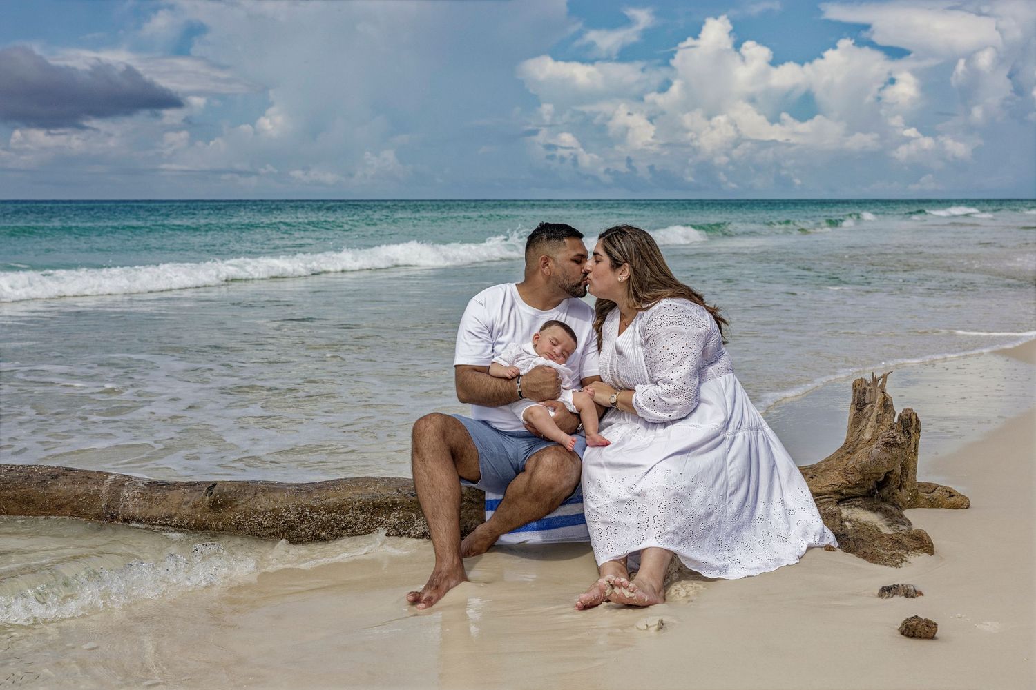 A romantic beach photoshoot series with a couple in white outfits sitting on rocks by the turquoise ocean.