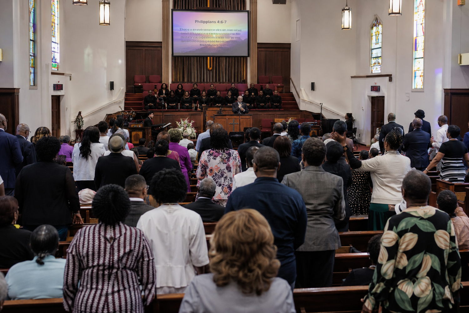 Congregation standing in prayer during a church service with choir and altar visible in a traditional sanctuary.