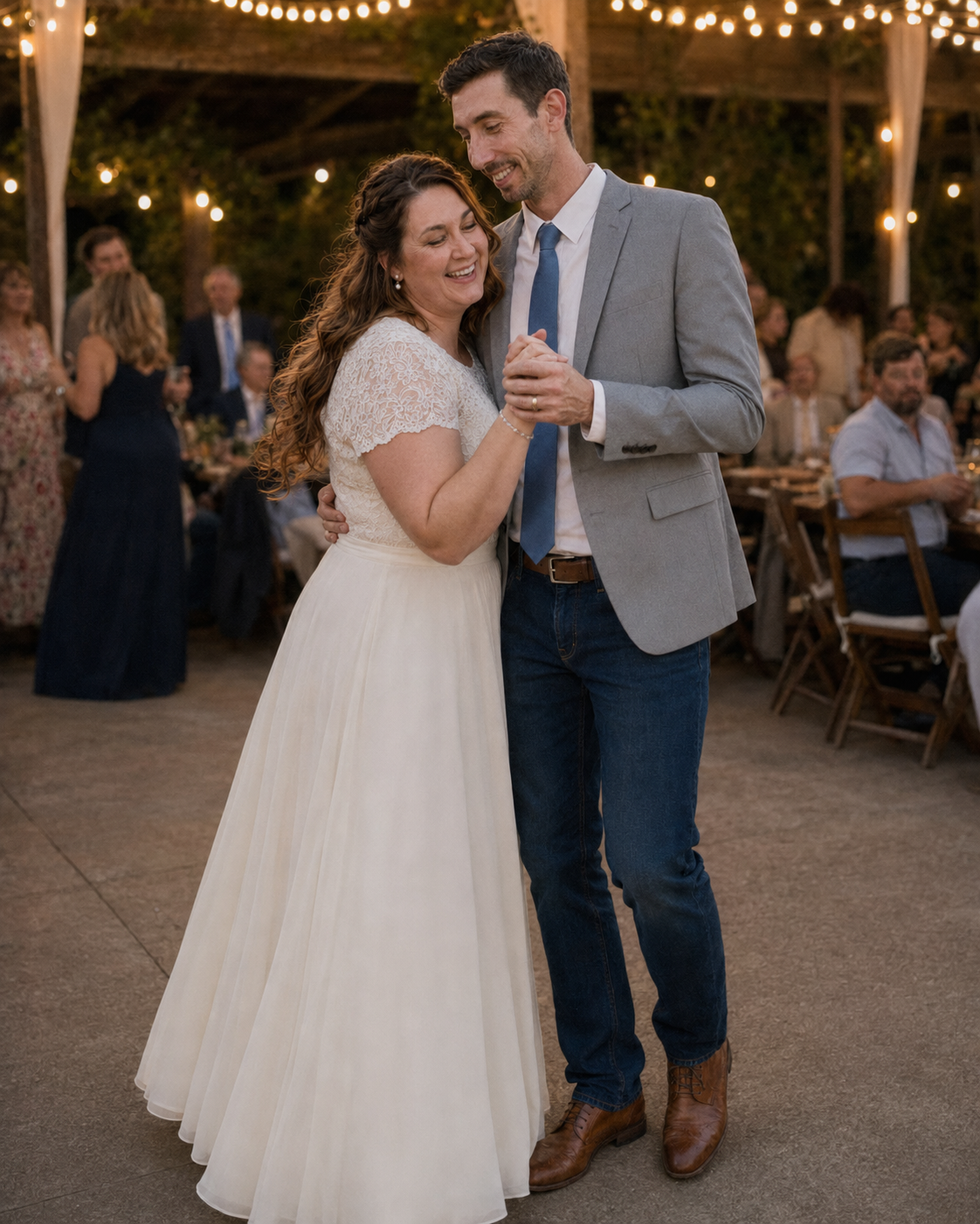 Bride and groom share a tender first dance under string lights at an outdoor rustic wedding reception.