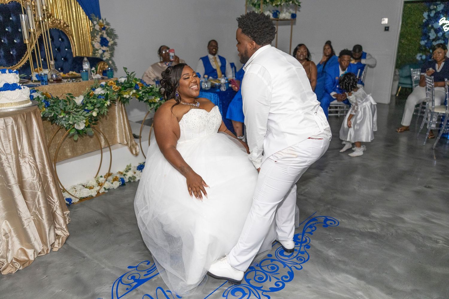 Bride and groom share a joyful first dance at their wedding reception with guests in blue attire seated nearby.